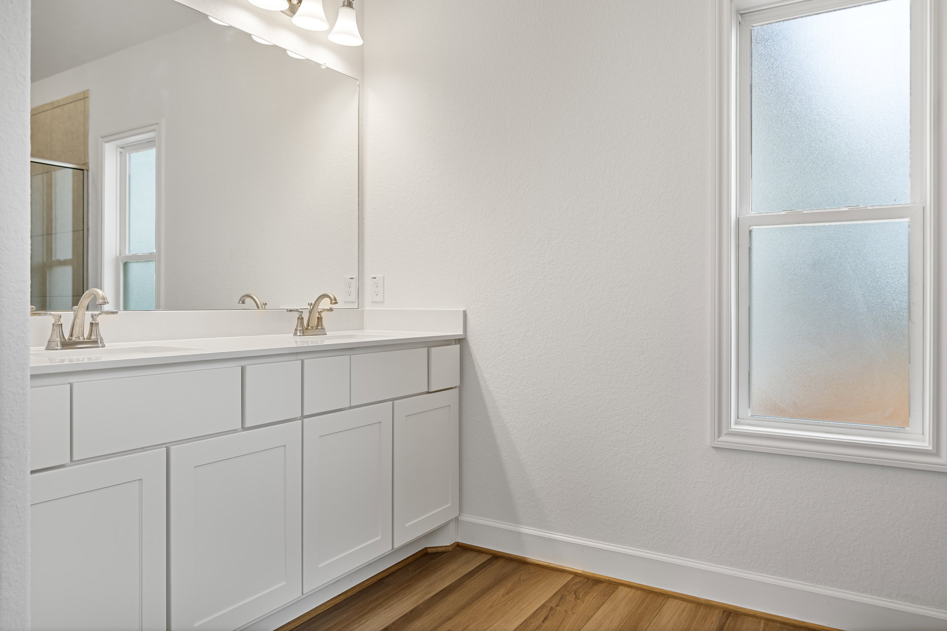Bathroom with wood flooring, frosted glass window, white cabinet with square panel, wall-mounted mirror above sink, white door in corner