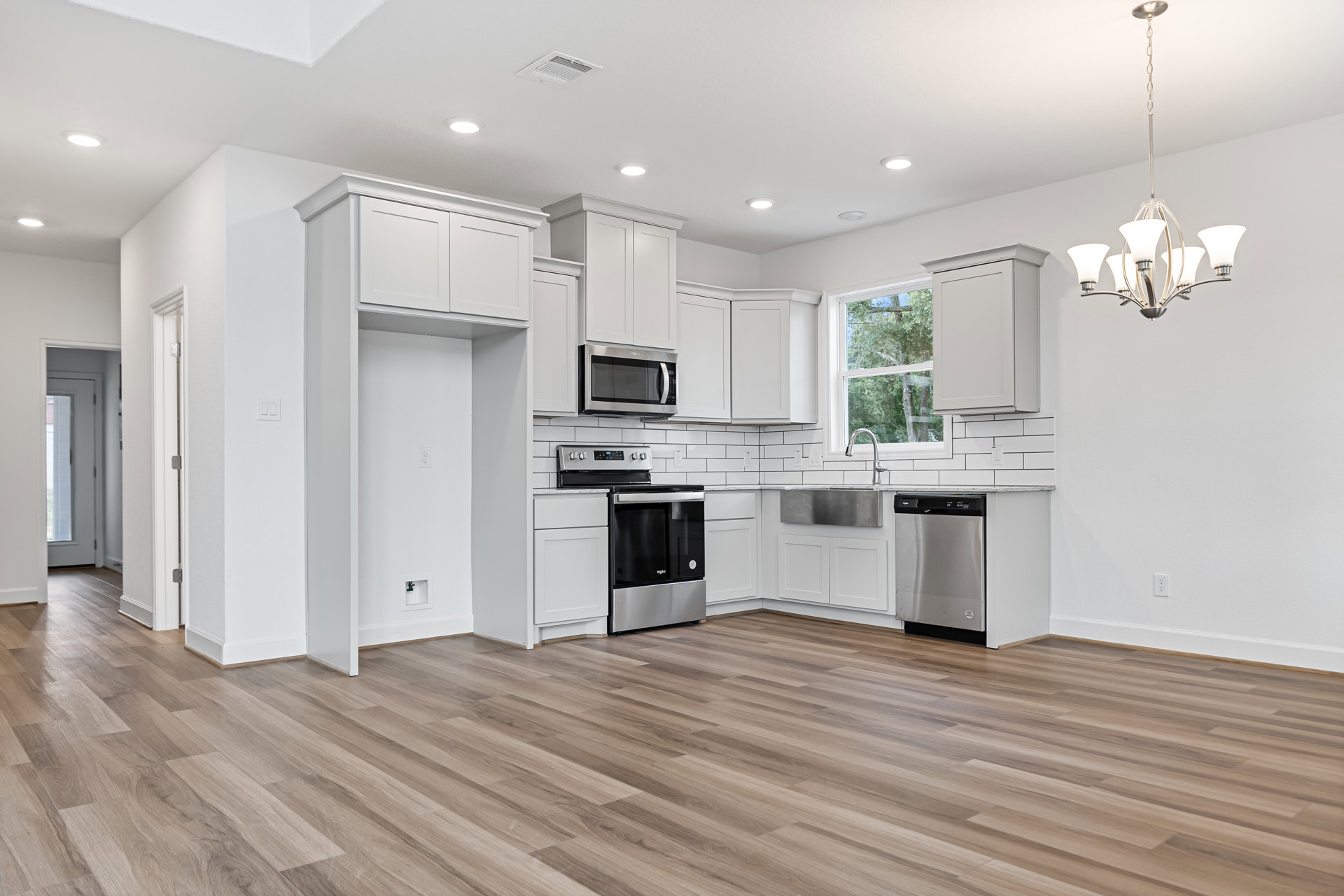White shaker cabinets, stainless steel appliances including microwave, oven, and dishwasher, wood flooring, stone countertops, and pendant lighting in a modern kitchen.
