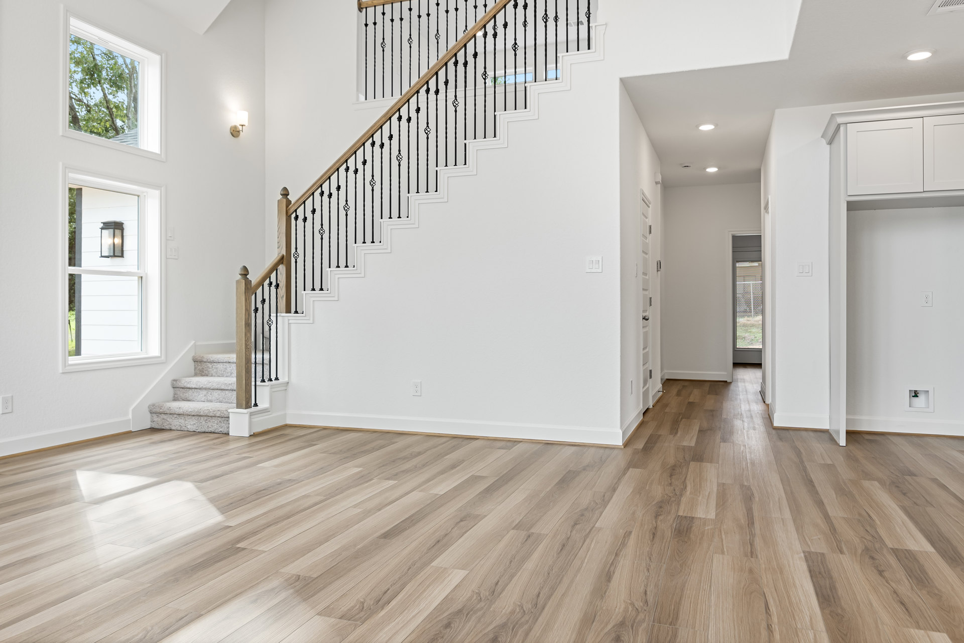 White staircase with black railings, wood flooring, white walls, wall sconce, window showing trees outside