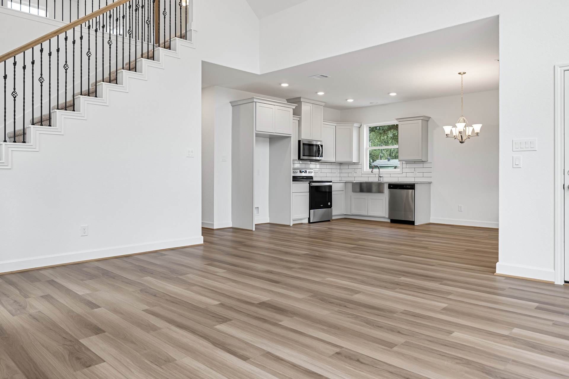 Open kitchen with white walls, wood flooring, black stove, built-in microwave, metal-railed staircase, and ceiling chandelier.