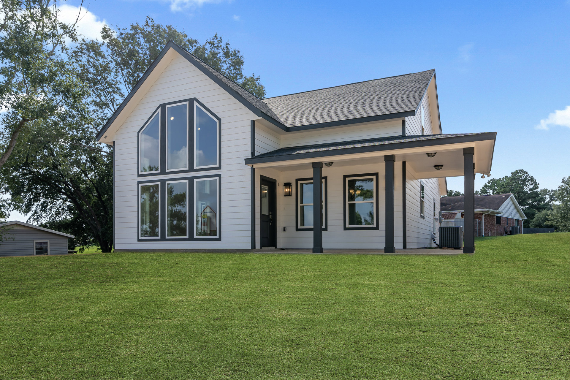 White and grey two-story house with black roof, multiple windows, covered porch, and green lawn under partly cloudy sky