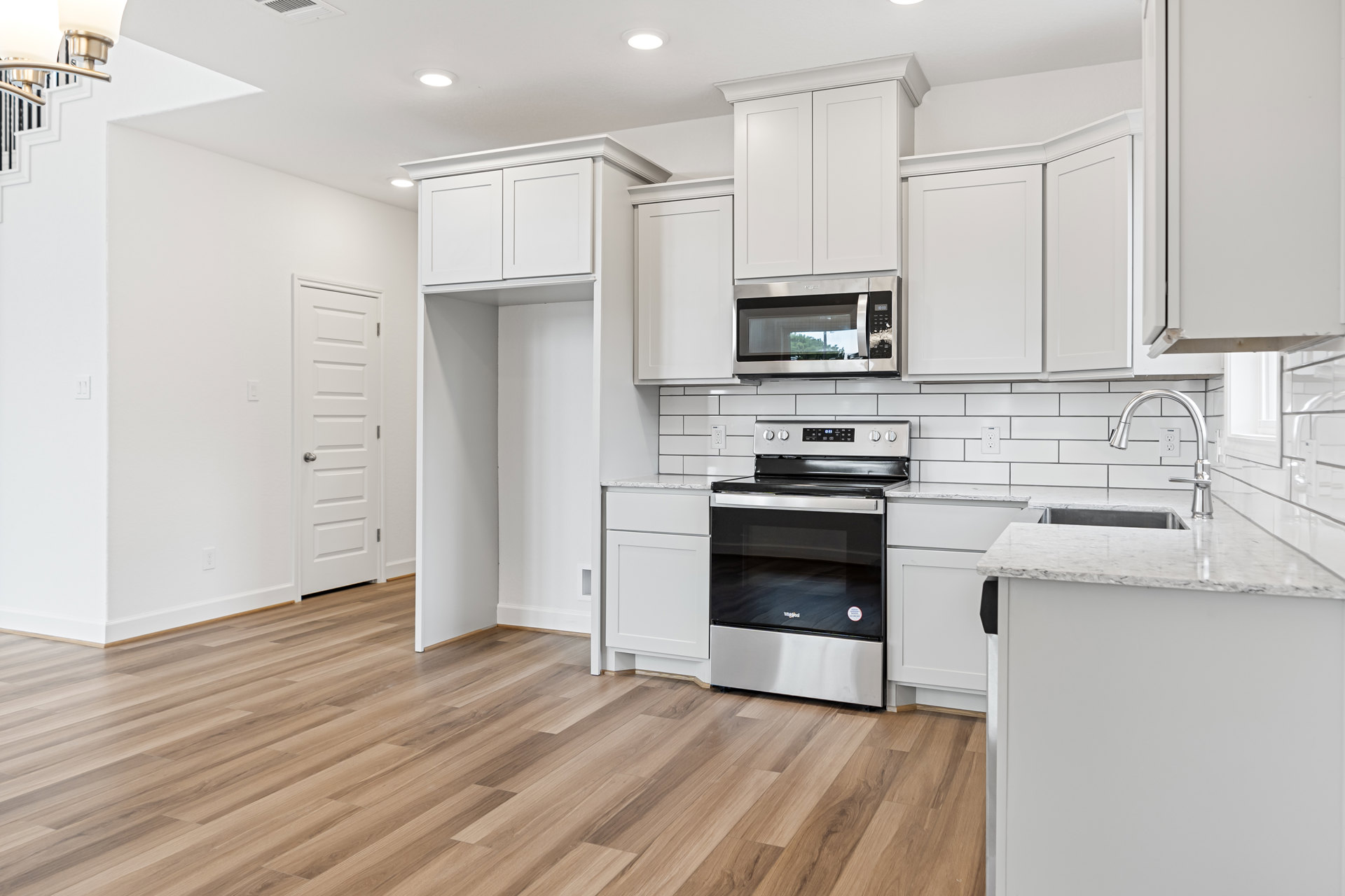 White kitchen cabinets, wood plank flooring, stainless steel stove and microwave, white doors with silver and black hardware, white countertops, built-in sink.