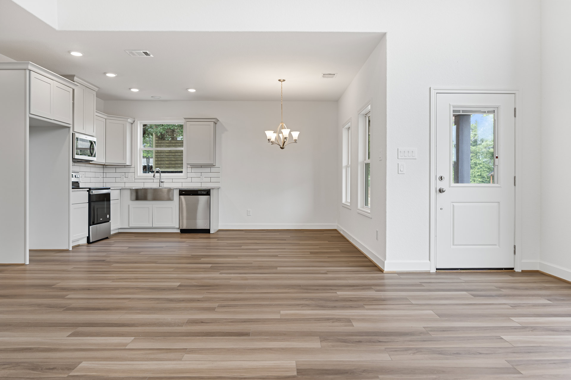 White kitchen with wood flooring, white cabinetry, stainless steel appliances including black oven, microwave, and dishwasher, glass windowed door, ceiling light fixture