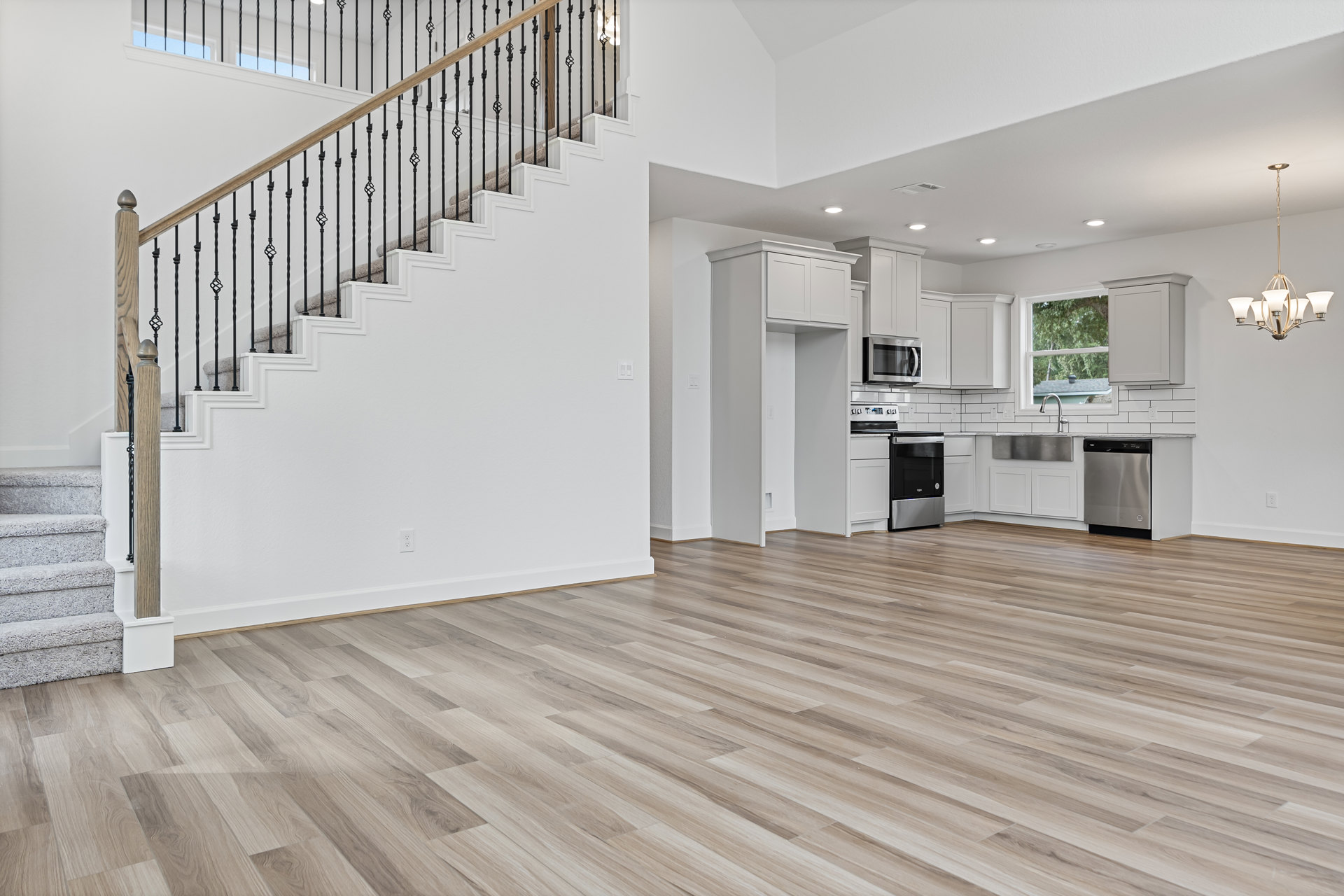 Open-concept interior featuring white walls, wood flooring, and a staircase with hardwood treads; modern kitchen appliances including a black and silver oven, microwave, and