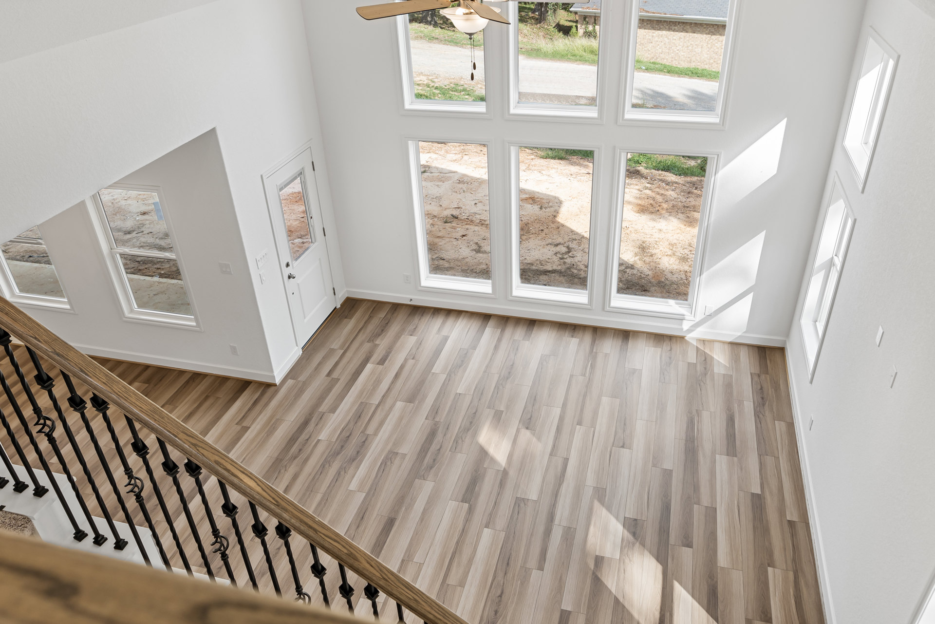 Wood floor room with black metal railing, white walls, ceiling fan, and staircase; window visible near corner.