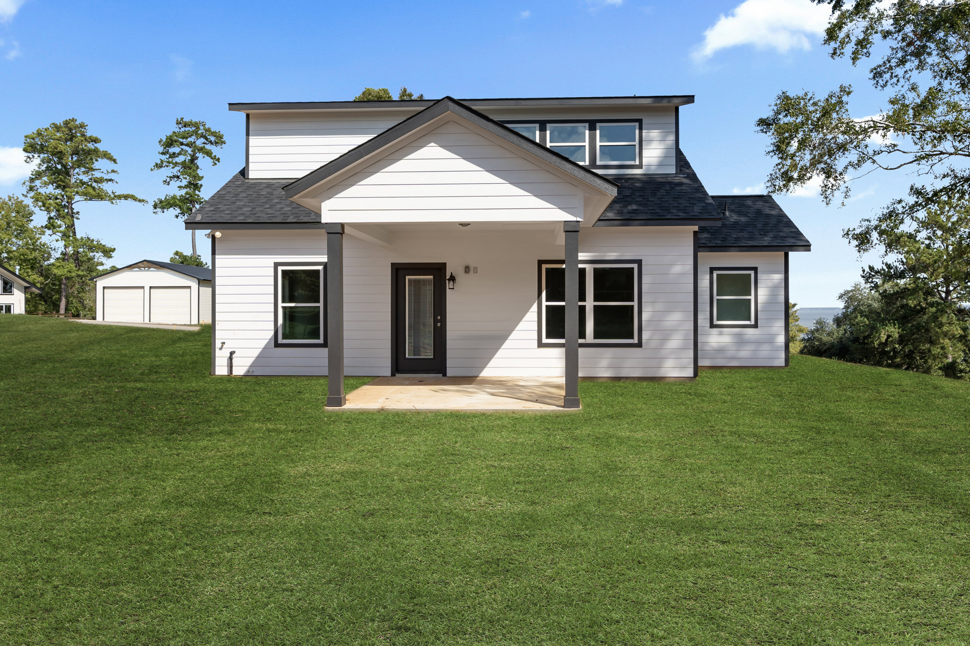 White siding house with black front door, covered porch with white columns, manicured green lawn, large windows with white frames, cloudy sky overhead