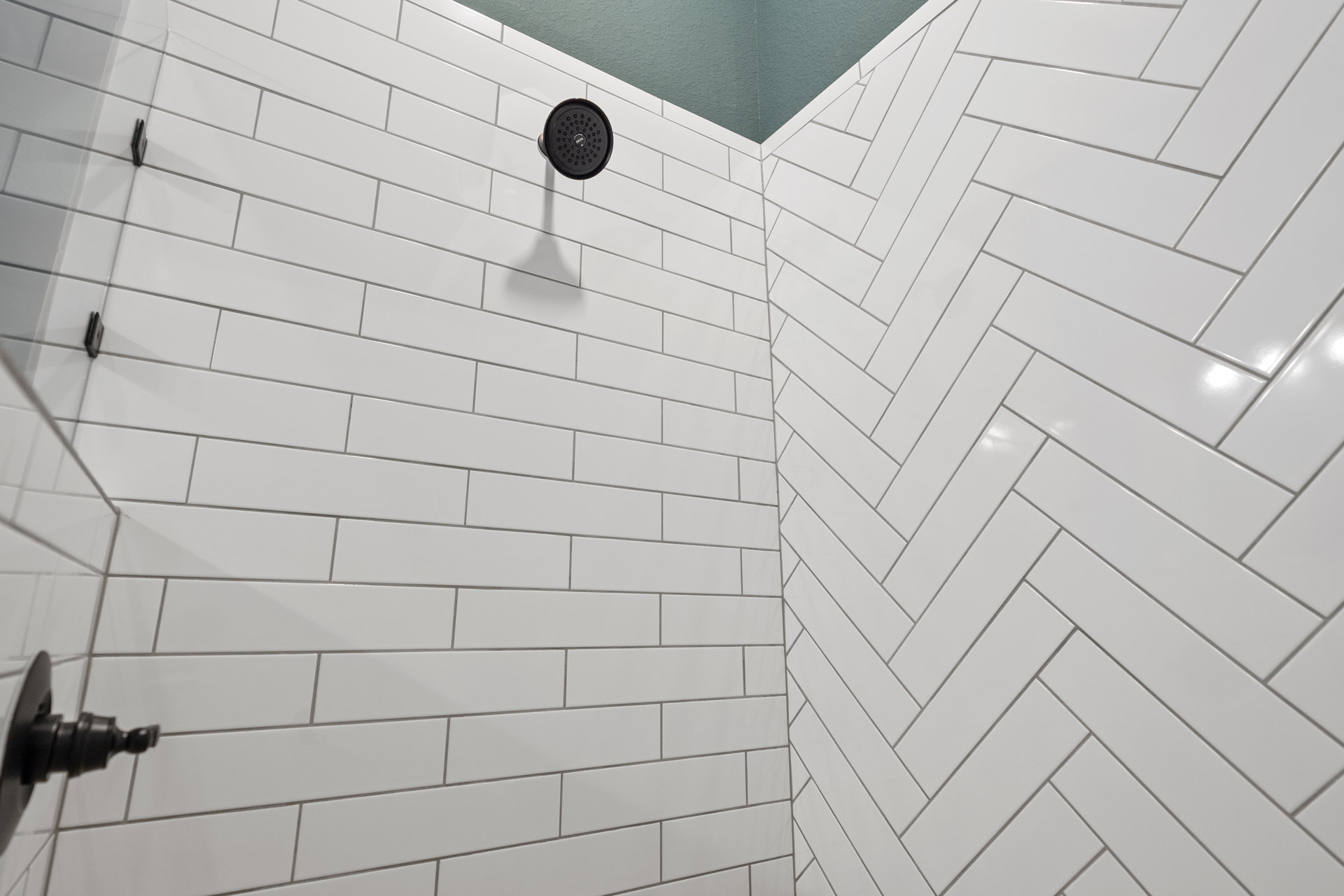 Matte black round shower head mounted on white tile wall in modern bathroom