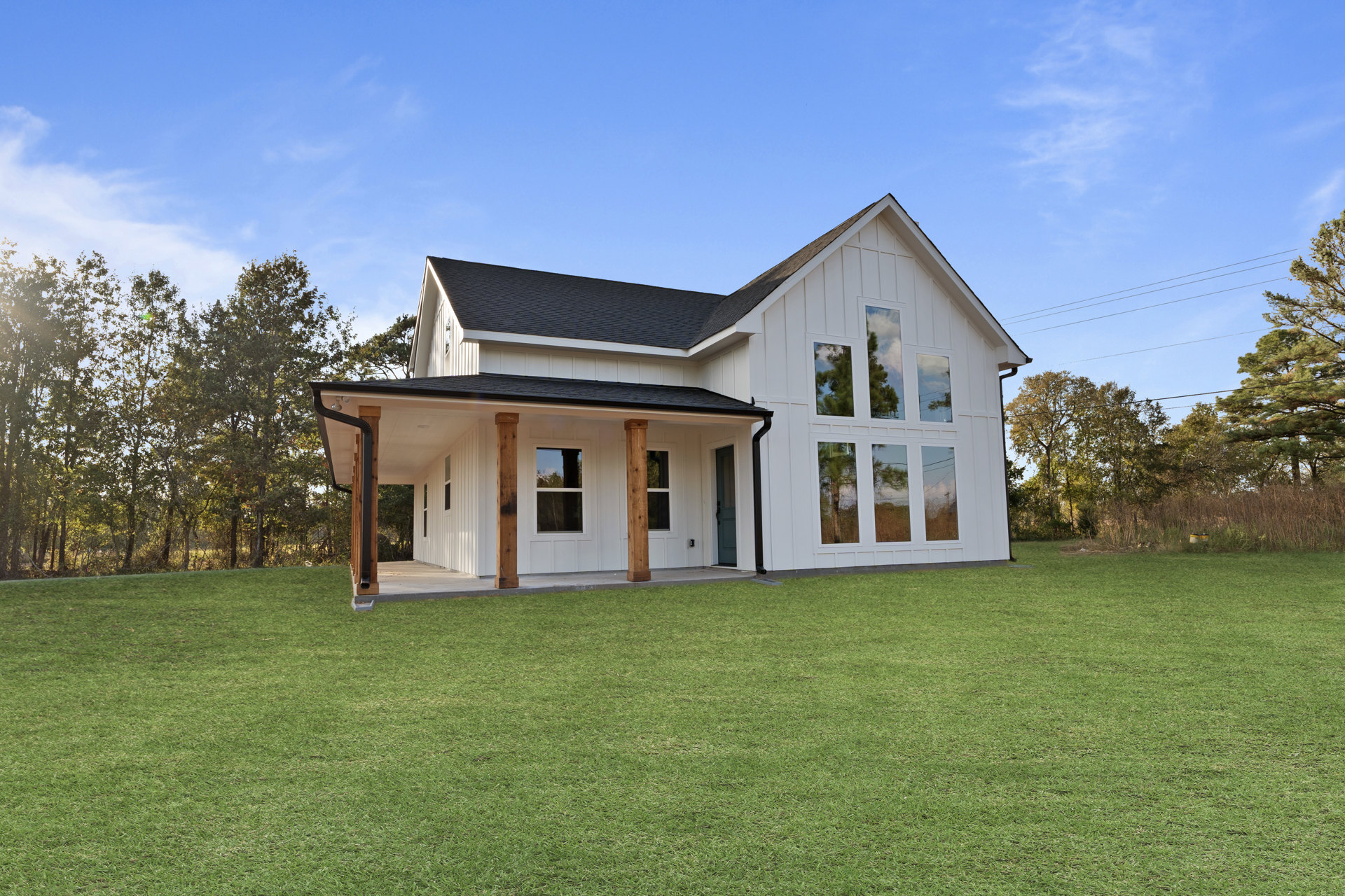 White house with wooden porch pillars, blue door and windows, surrounded by green lawn and trees under a partly cloudy sky