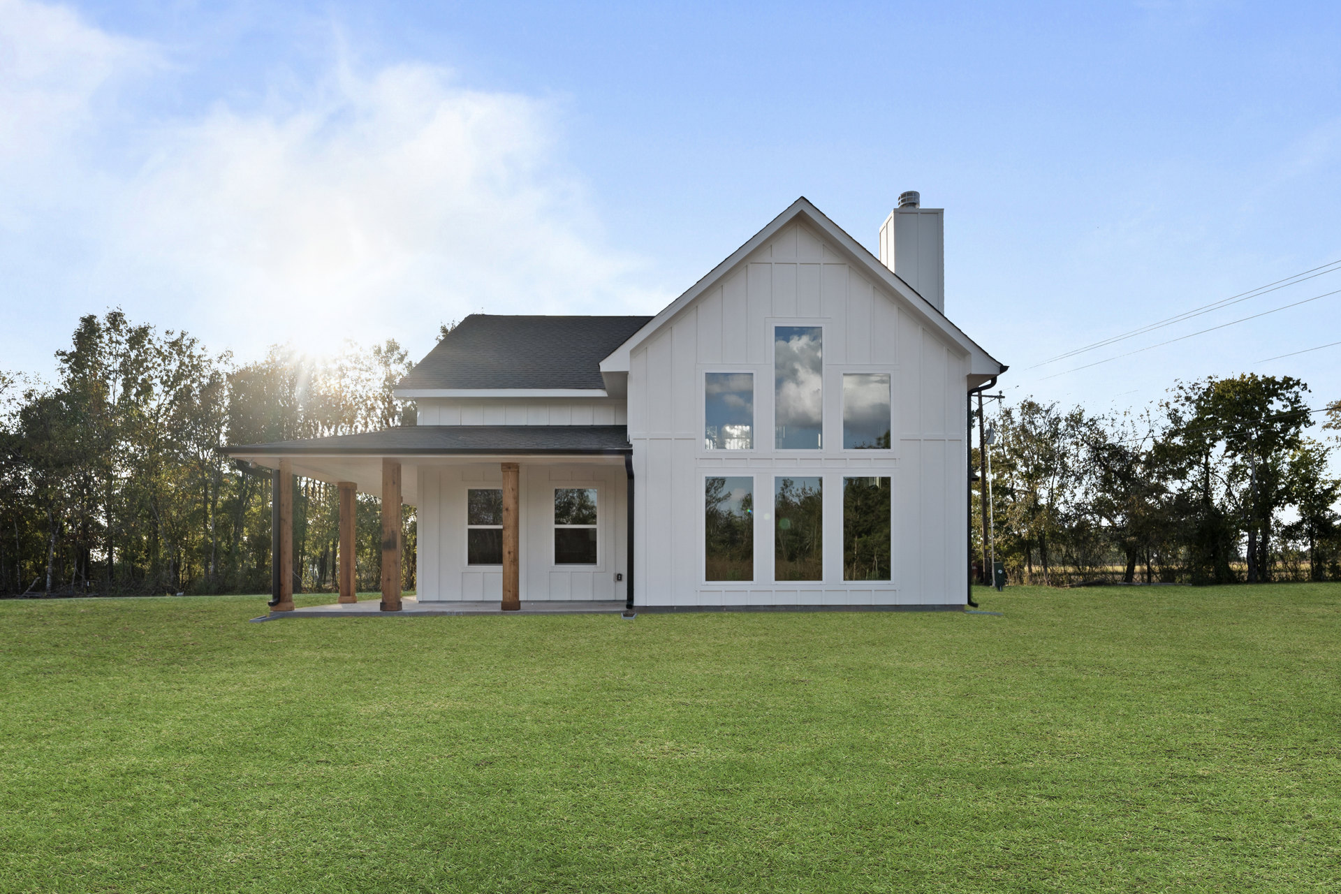 White house with black roof, wood pillars on porch, multiple windows, green lawn, blue sky with scattered clouds