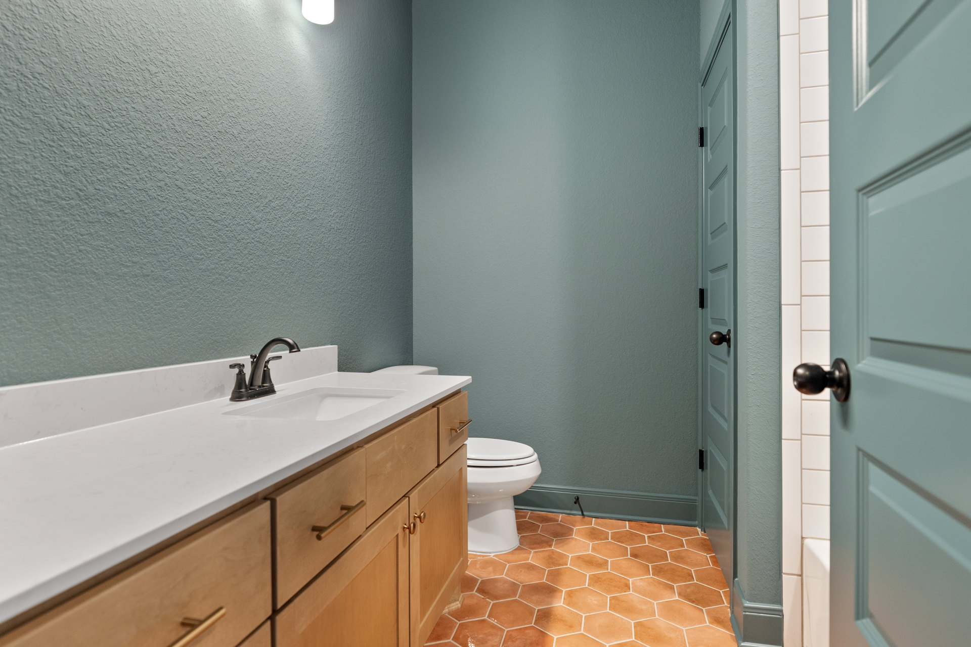 Bathroom with white toilet, modern sink and drawers, chrome faucet, tile flooring, and close-up of brushed metal door knob