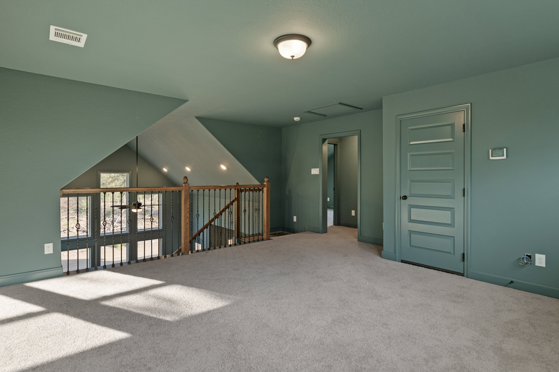 Carpeted room featuring a wooden staircase, white paneled door with a sign, ceiling fan, recessed light fixture, and white ceiling vent