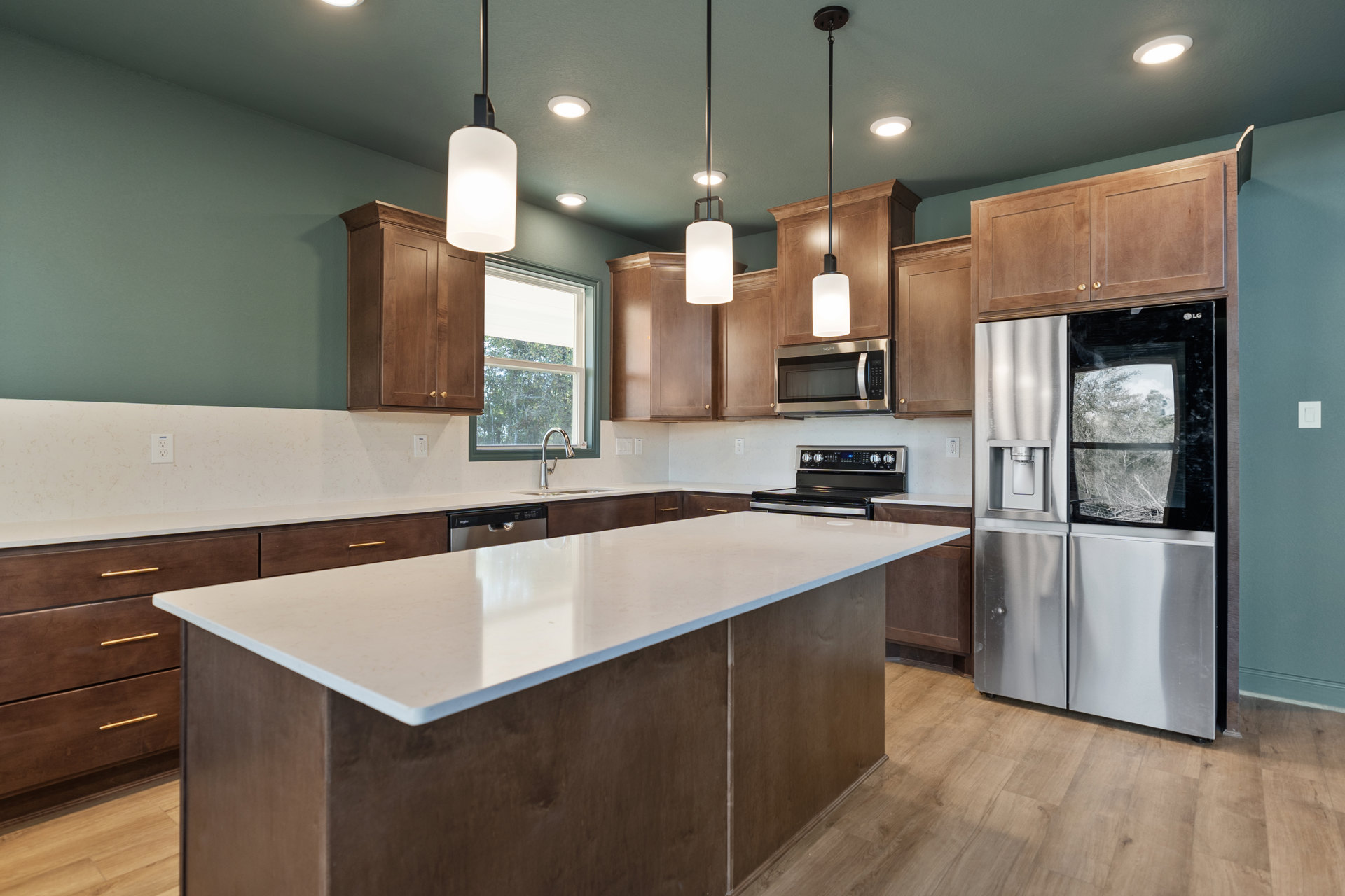 Kitchen with large white island, stainless steel appliances including refrigerator with water dispenser, microwave under ceiling light, white countertops, cabinetry, window