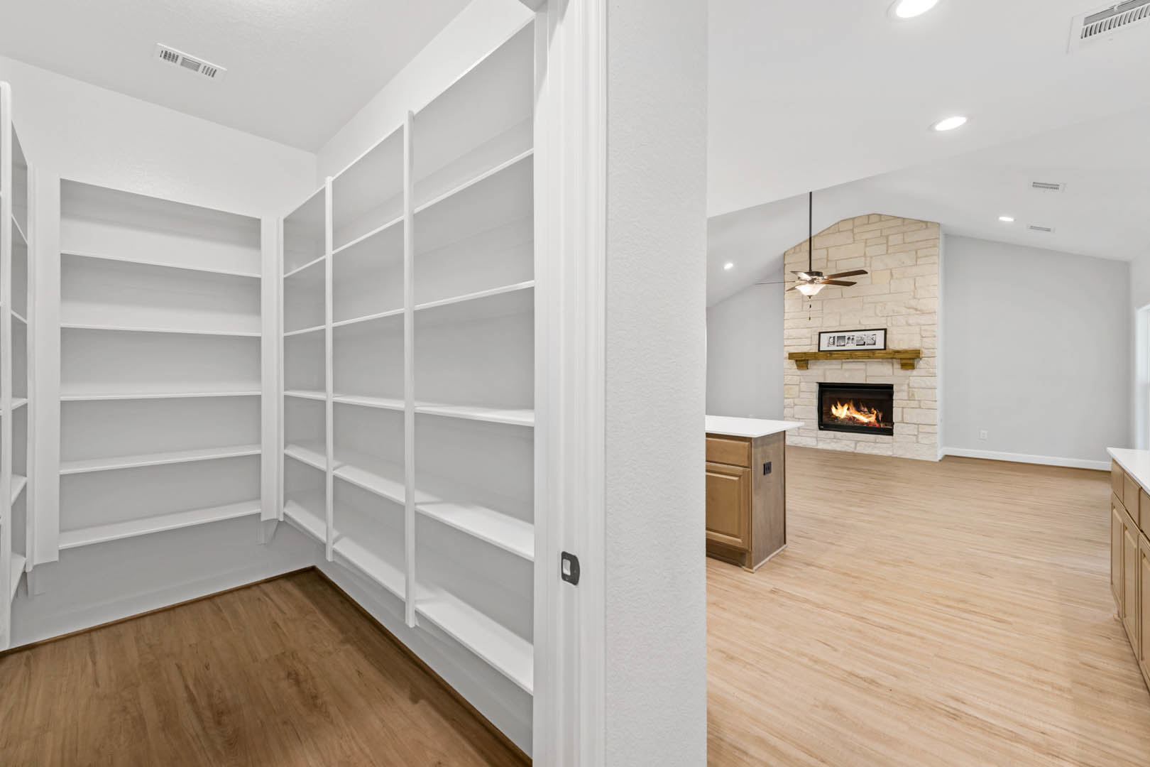 Hardwood floor with white baseboards, built-in white shelves flanking a fireplace with a burning fire, cabinetry detail visible, neutral wall tones