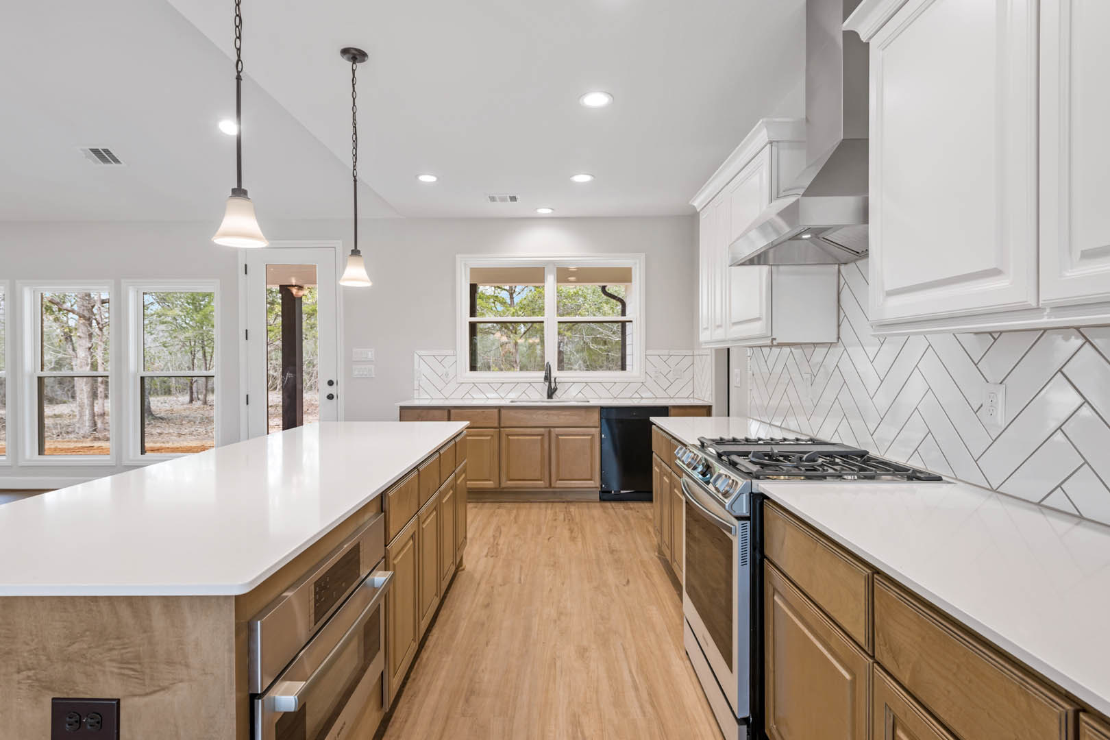 White kitchen with shaker cabinets, quartz countertops, stainless steel stove and oven, window overlooking trees, pendant light fixture, hardwood flooring