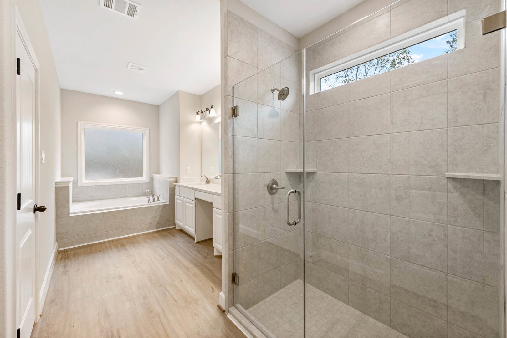 Bathroom with glass shower enclosure, freestanding tub, frosted glass window, wood flooring, white plaster walls, and chrome shower knob