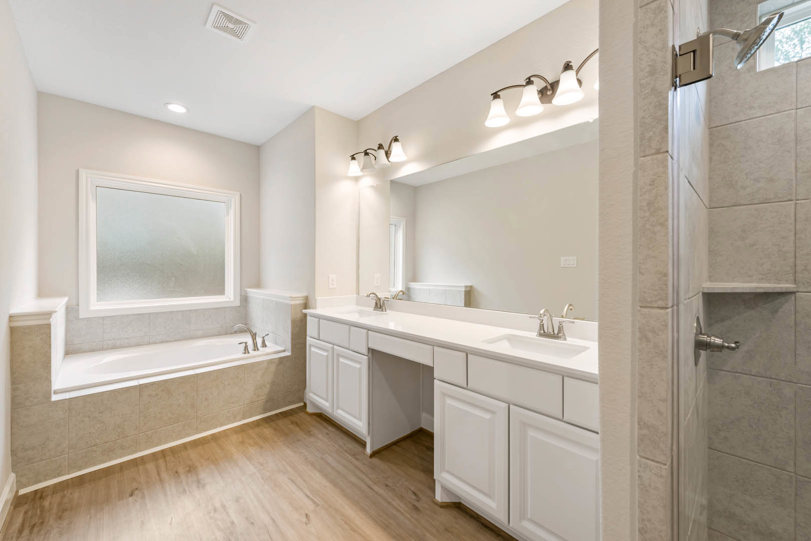 Bathroom with freestanding white bathtub, rectangular sink on stone countertop, frosted glass window in white frame, three-light fixture above large mirror, tiled floor and walls