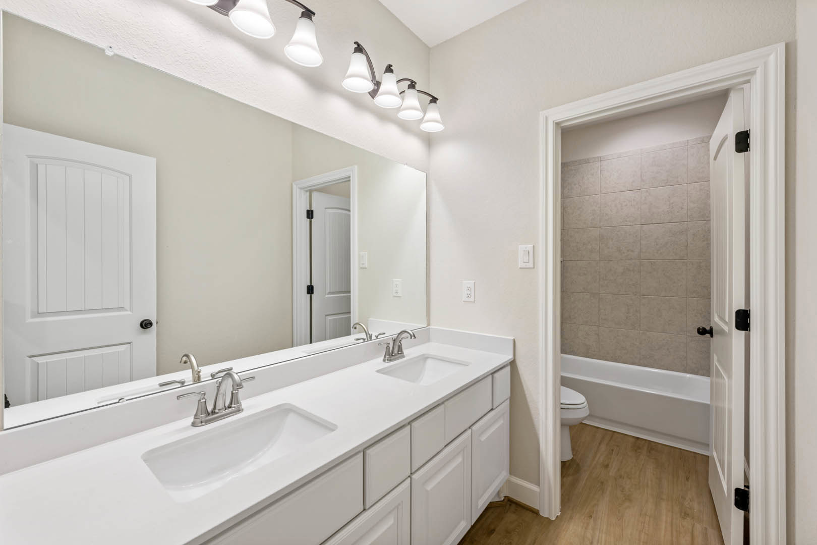 White bathroom with shaker cabinets, freestanding bathtub, silver faucet, four-light fixture, and paneled door