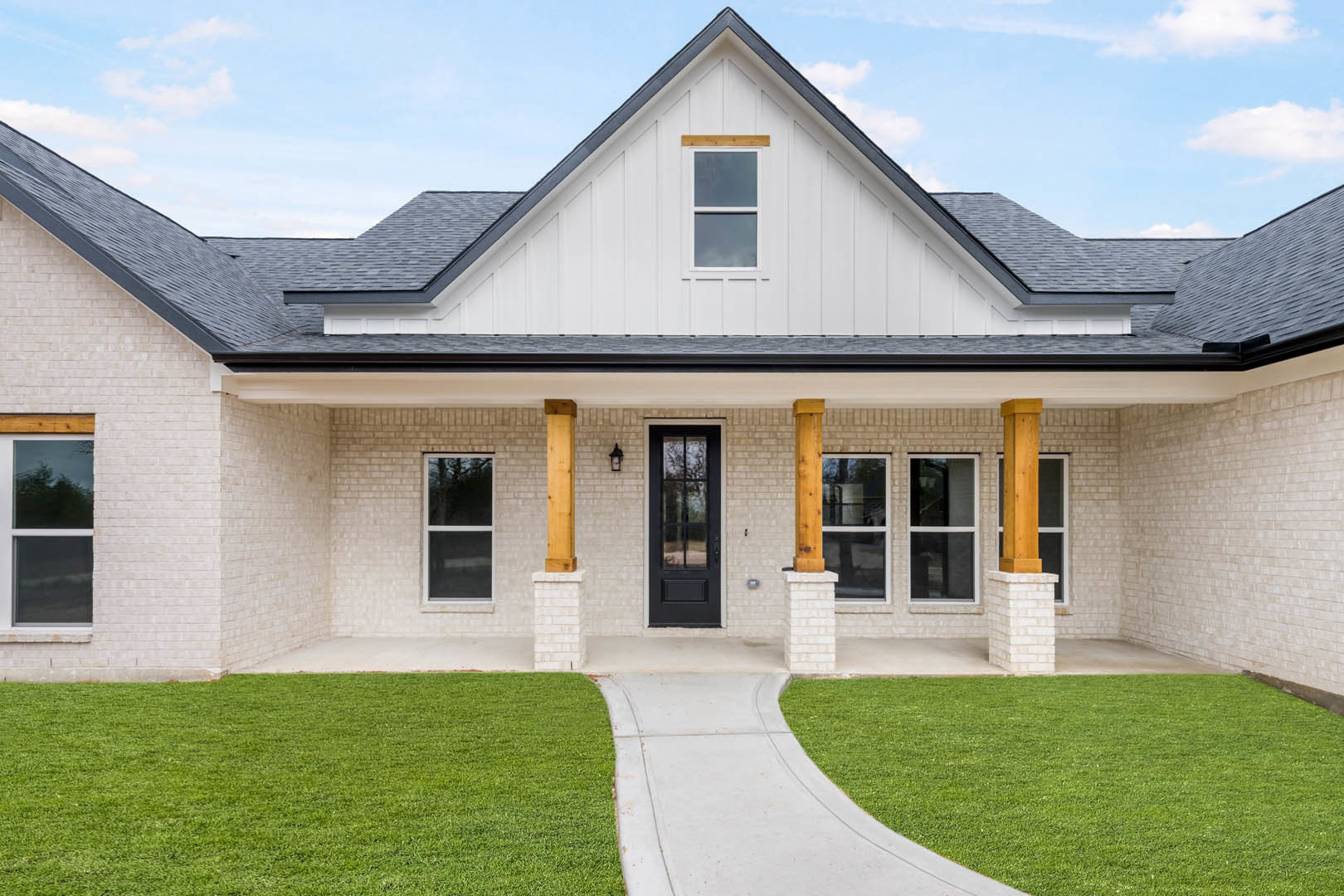 White house with black front door, white-framed windows, green lawn, concrete walkway, and small porch.
