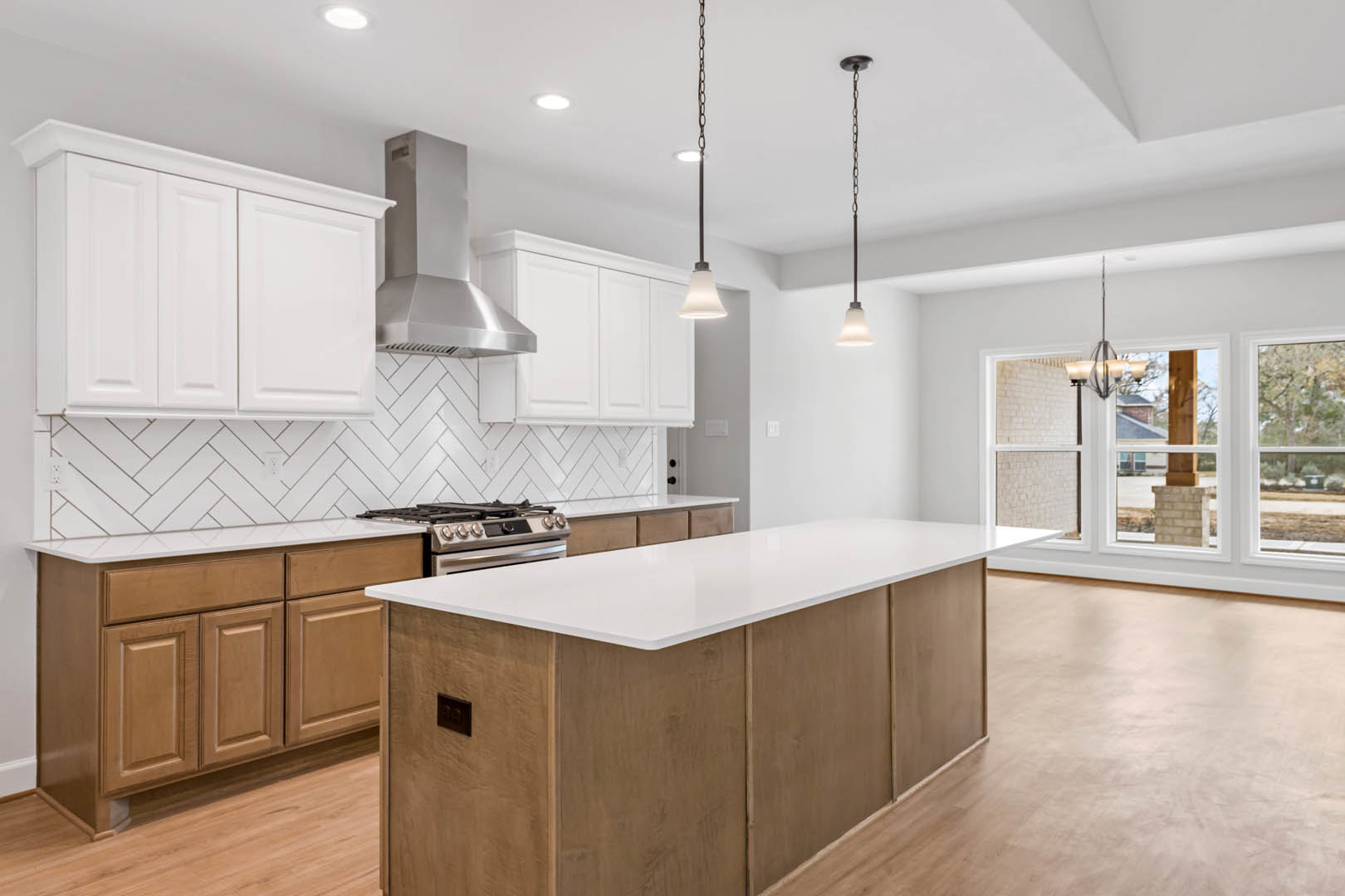 Spacious kitchen featuring a large white island with built-in stove and oven, white cabinetry, tile backsplash, black rectangular electrical outlet, and chain hanging from a pole