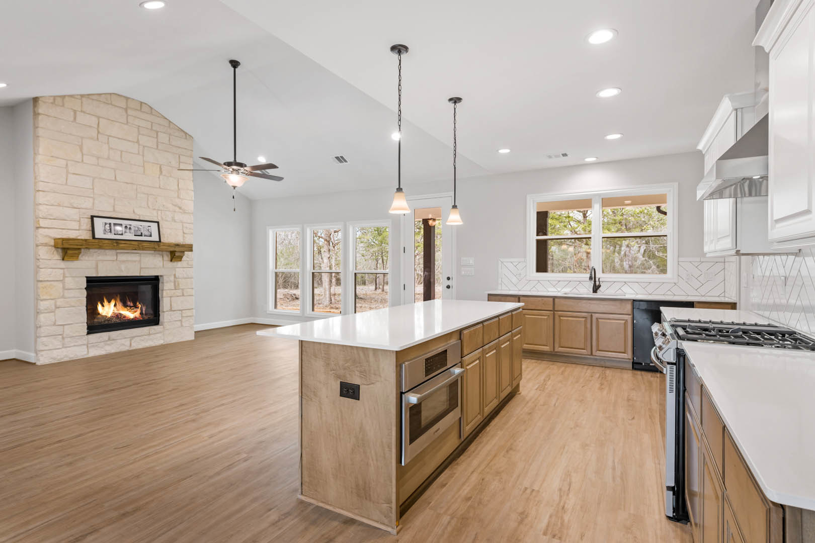 Spacious kitchen featuring a stone fireplace with active fire, large central island with quartz countertop, white cabinetry, stainless steel appliances including microwave