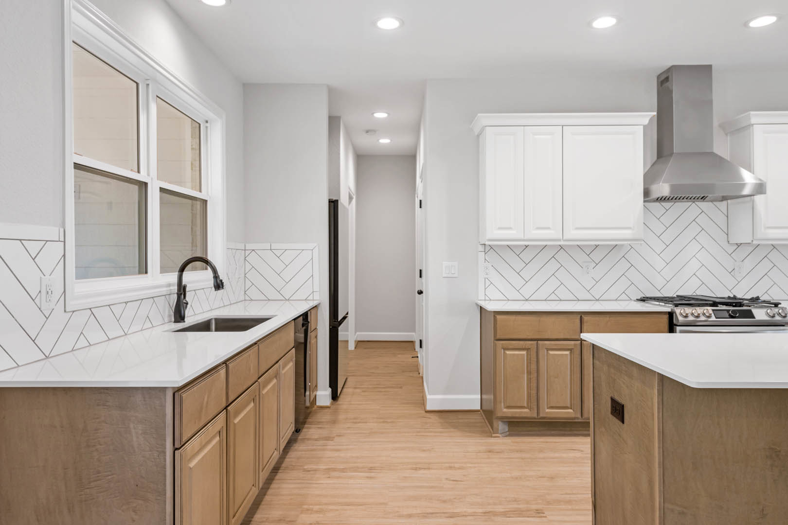 Kitchen with white shaker cabinets, wood plank flooring, white quartz countertops, stainless steel vent hood, chrome faucet, and a window with a white frame