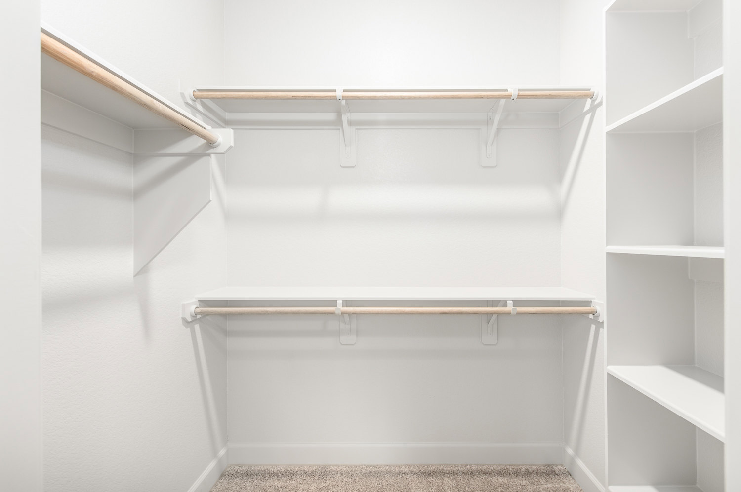 White closet with built-in shelves, wooden hanging rod, and carpeted floor.