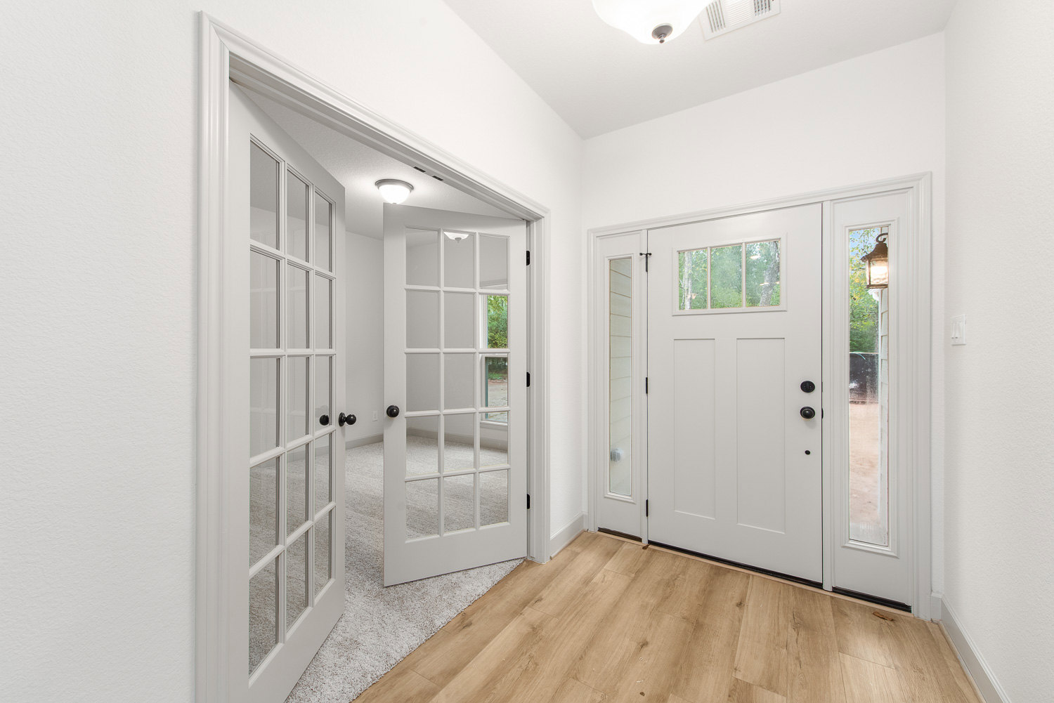 White double doors with glass panels, wood flooring, white walls, and a window showing trees outside