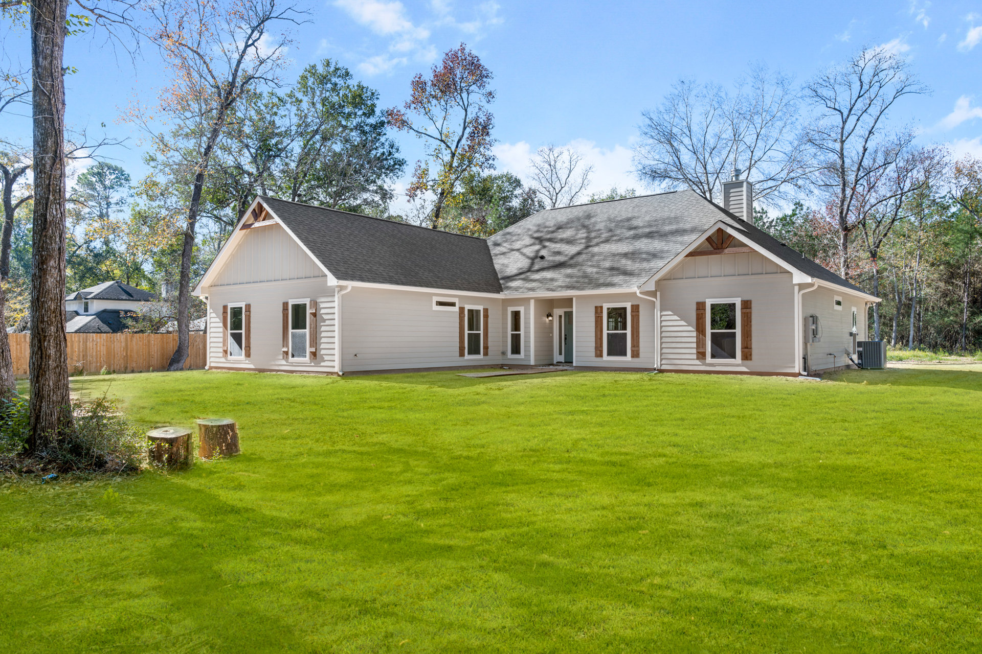Two-story farmhouse with white siding and large windows, surrounded by a green lawn and mature trees under a partly cloudy sky
