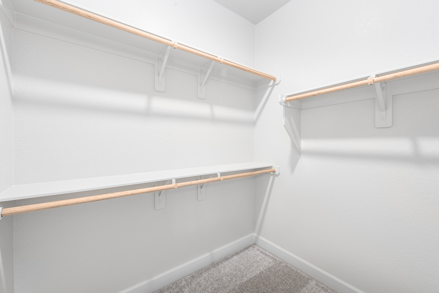 White closet with built-in shelves, wooden hanging bar, white metal brackets, carpeted floor, and plaster walls.