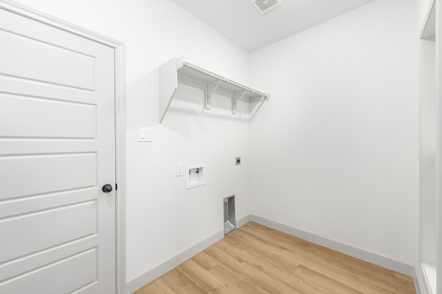 White room with wood flooring, white door, built-in shelf, and white trim