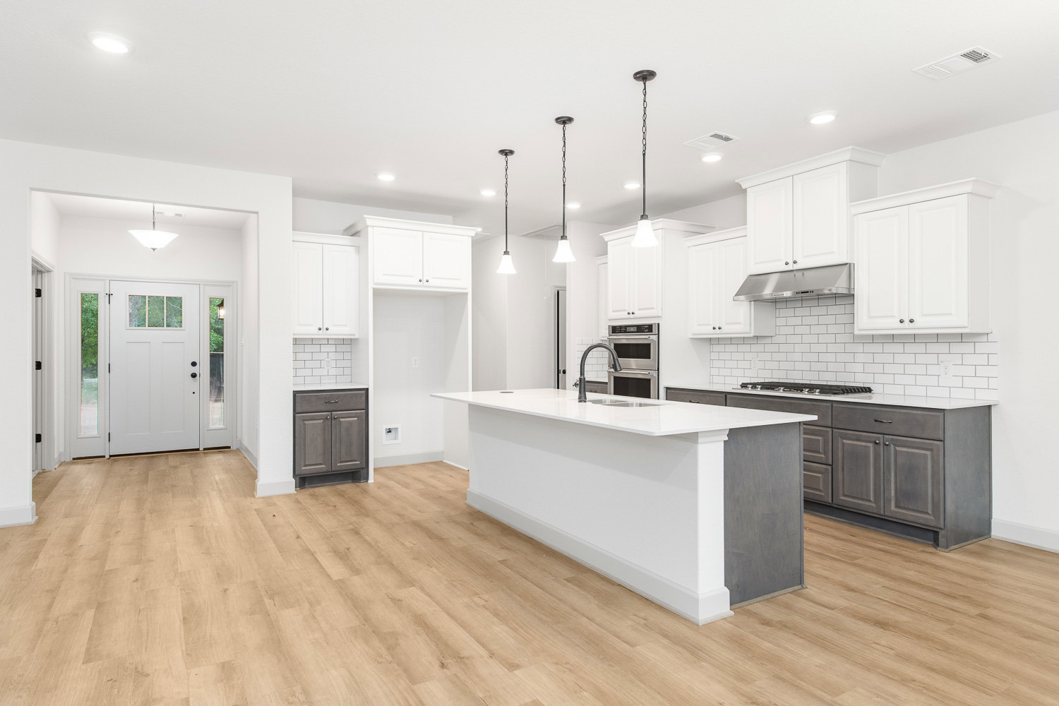 Open kitchen with wood flooring, white cabinets with silver knobs, white island topped with a black appliance, glass-paneled door, and stainless steel sink