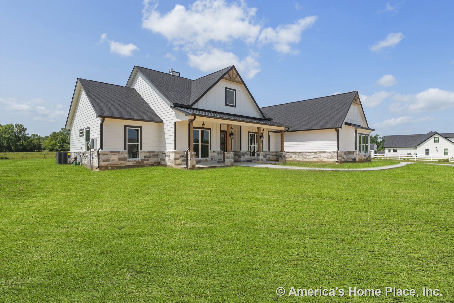White siding and stone trim exterior with black shingle roof, covered front porch supported by columns, multiple large windows, outdoor lighting fixtures, and a spacious front