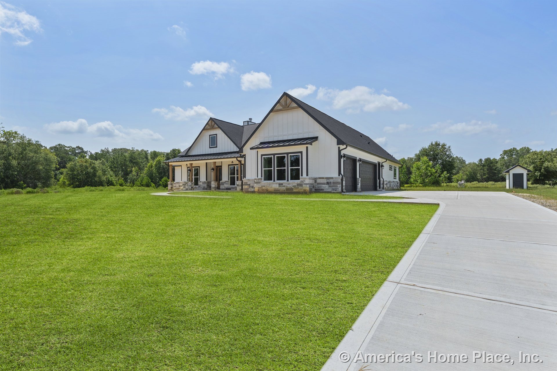 Board and batten siding with stone trim base, black shingle roof, three-car garage doors, large windows, covered front porch supported by columns, concrete driveway, rural setting