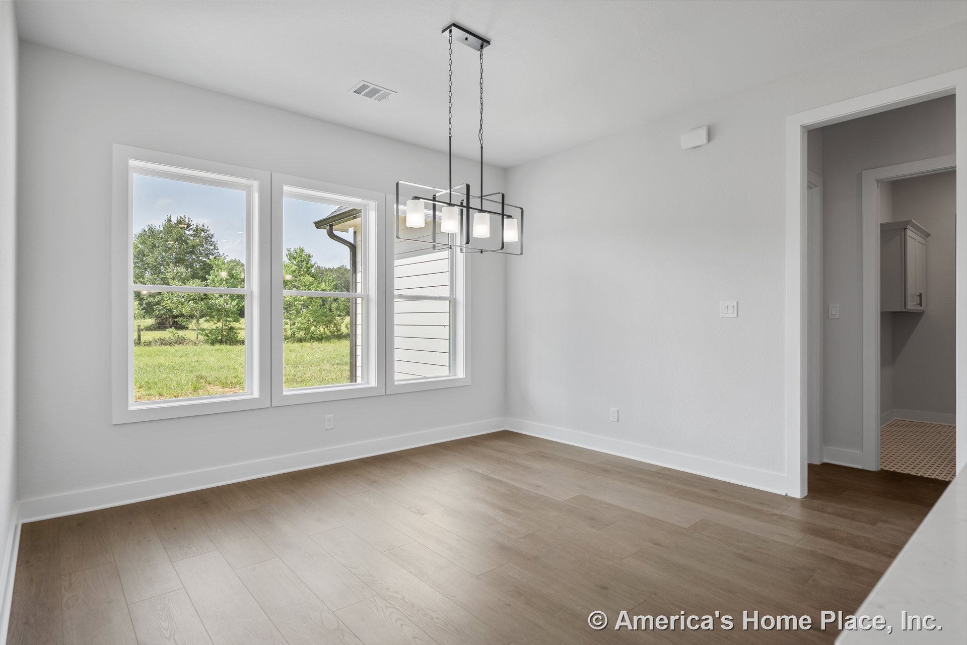 Dining area with three-pane windows, light wood plank flooring, white baseboards, modern rectangular ceiling chandelier, open doorway to adjacent room, and smooth white walls.