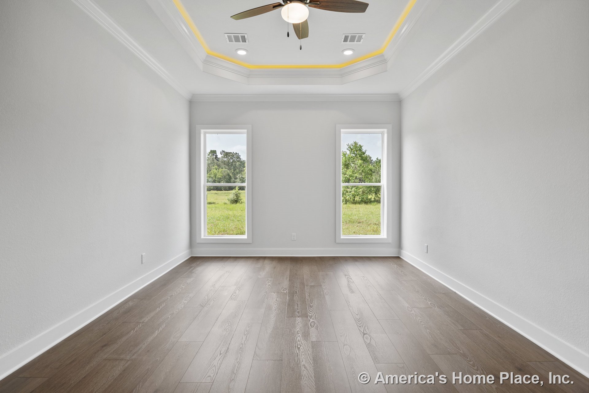 Tray ceiling with accent lighting and recessed lights, ceiling fan fixture, two tall windows allowing natural light, wood plank flooring, white baseboards and trim, empty room with