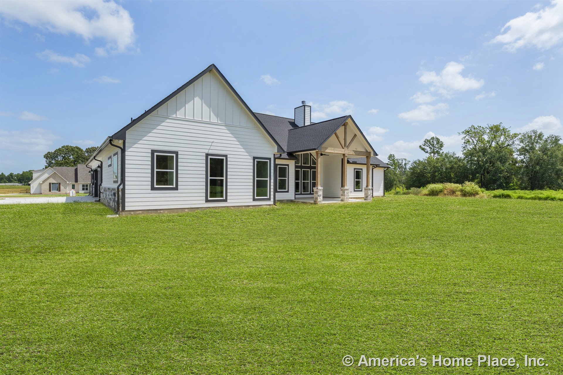 White vertical siding with black trim windows, covered front porch supported by stone column bases, multiple windows, and prominent gable roof.