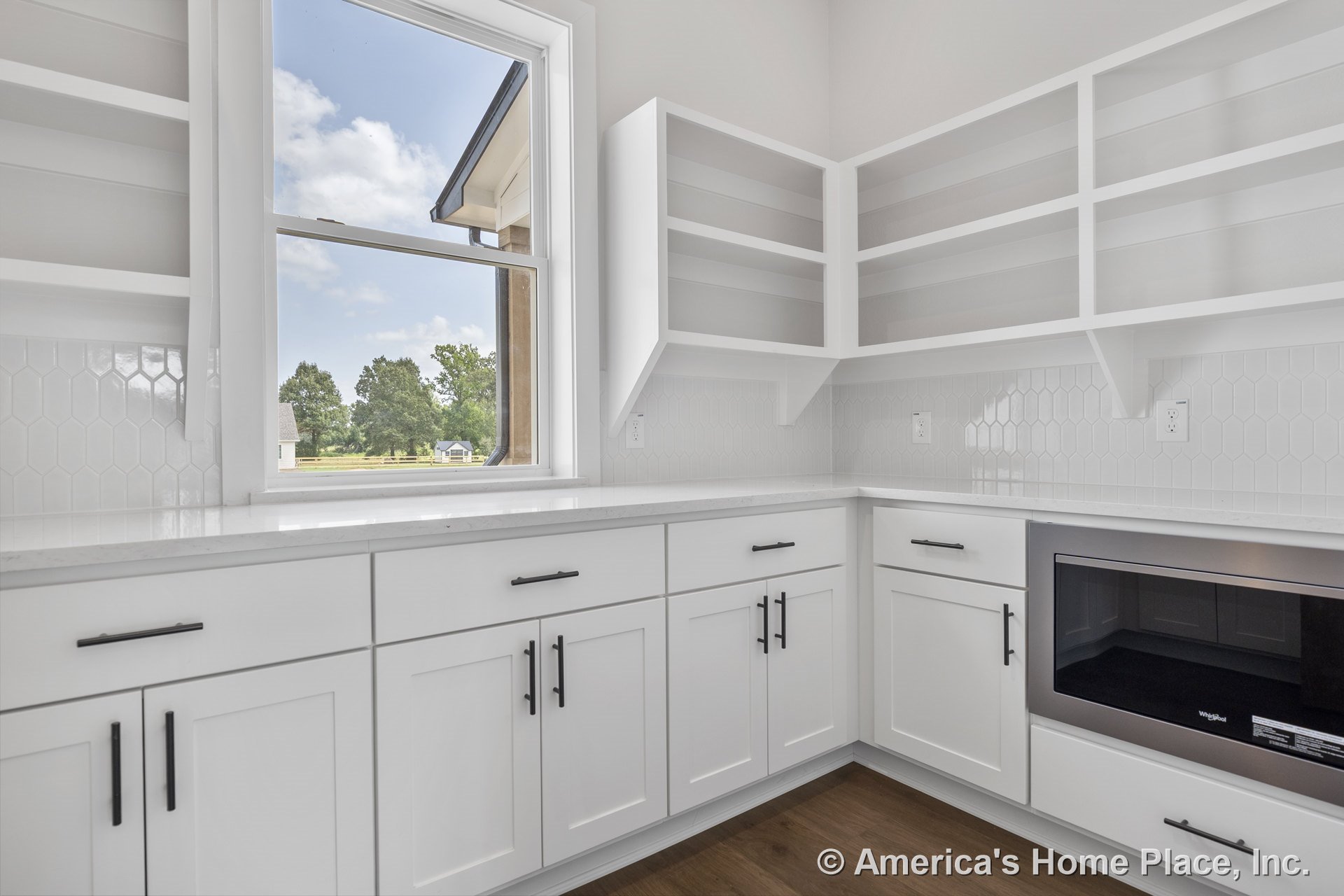 White shaker cabinets with modern hardware, open upper shelving, hexagonal tile backsplash, built-in microwave, quartz countertops, wood flooring, and white trim beneath a large