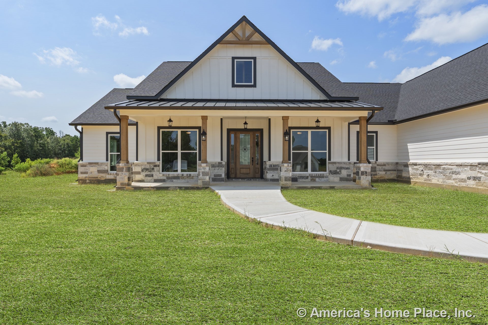 Covered front porch with stone and wood columns, board and batten siding, large windows, decorative glass entry door, architectural gable trim, exterior lighting, and paved