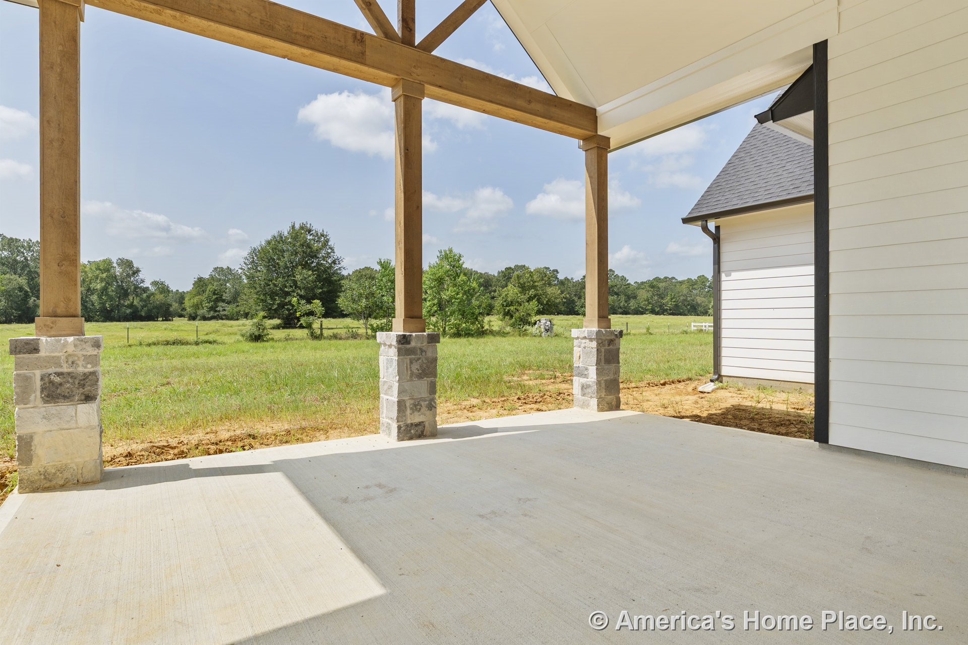 Covered porch with exposed wood ceiling beams, stone column bases, concrete floor, white siding exterior, and open gable roof.