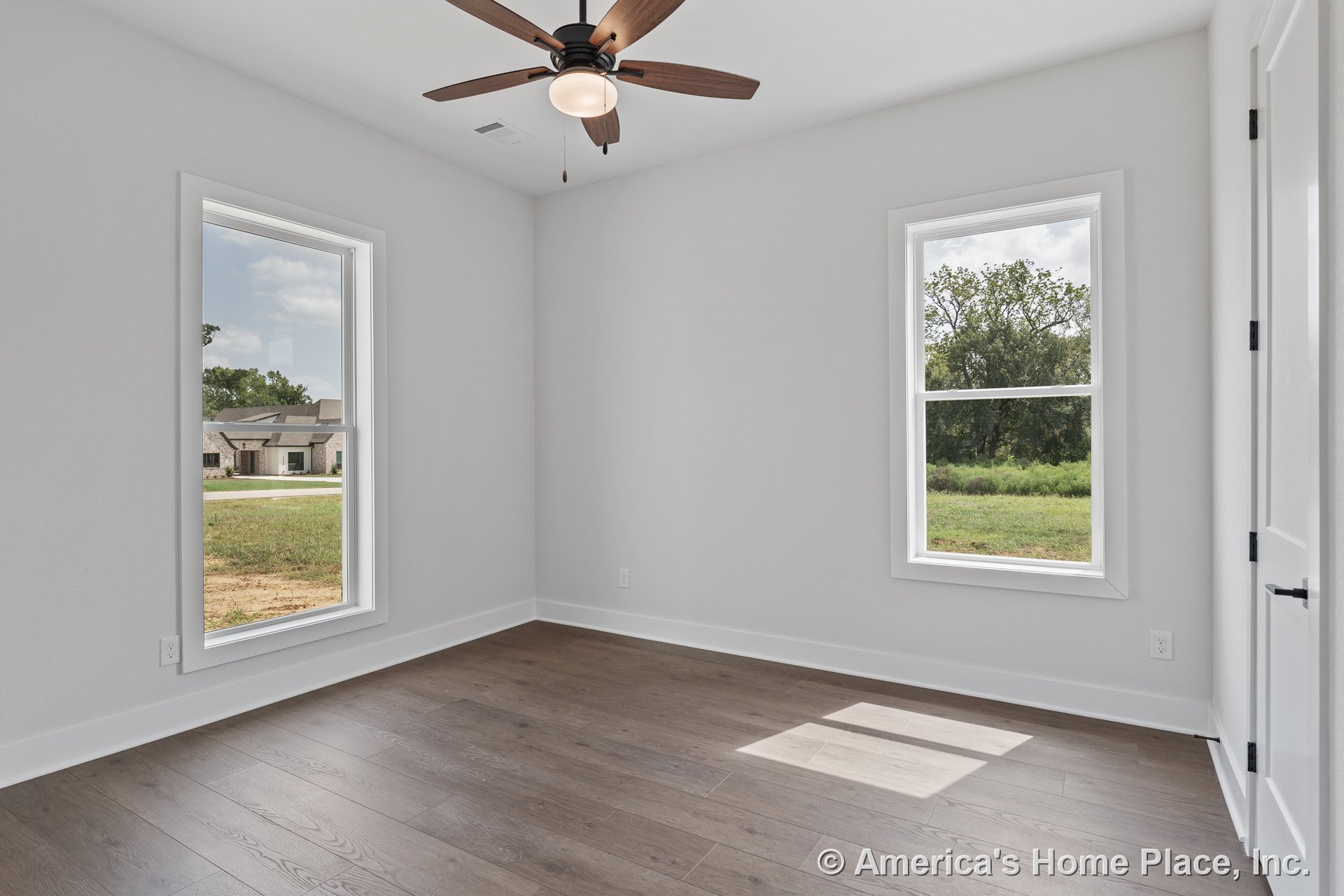 Bedroom with double windows, wood plank flooring, white trim and baseboards, neutral painted walls, ceiling fan with integrated light, and interior door.