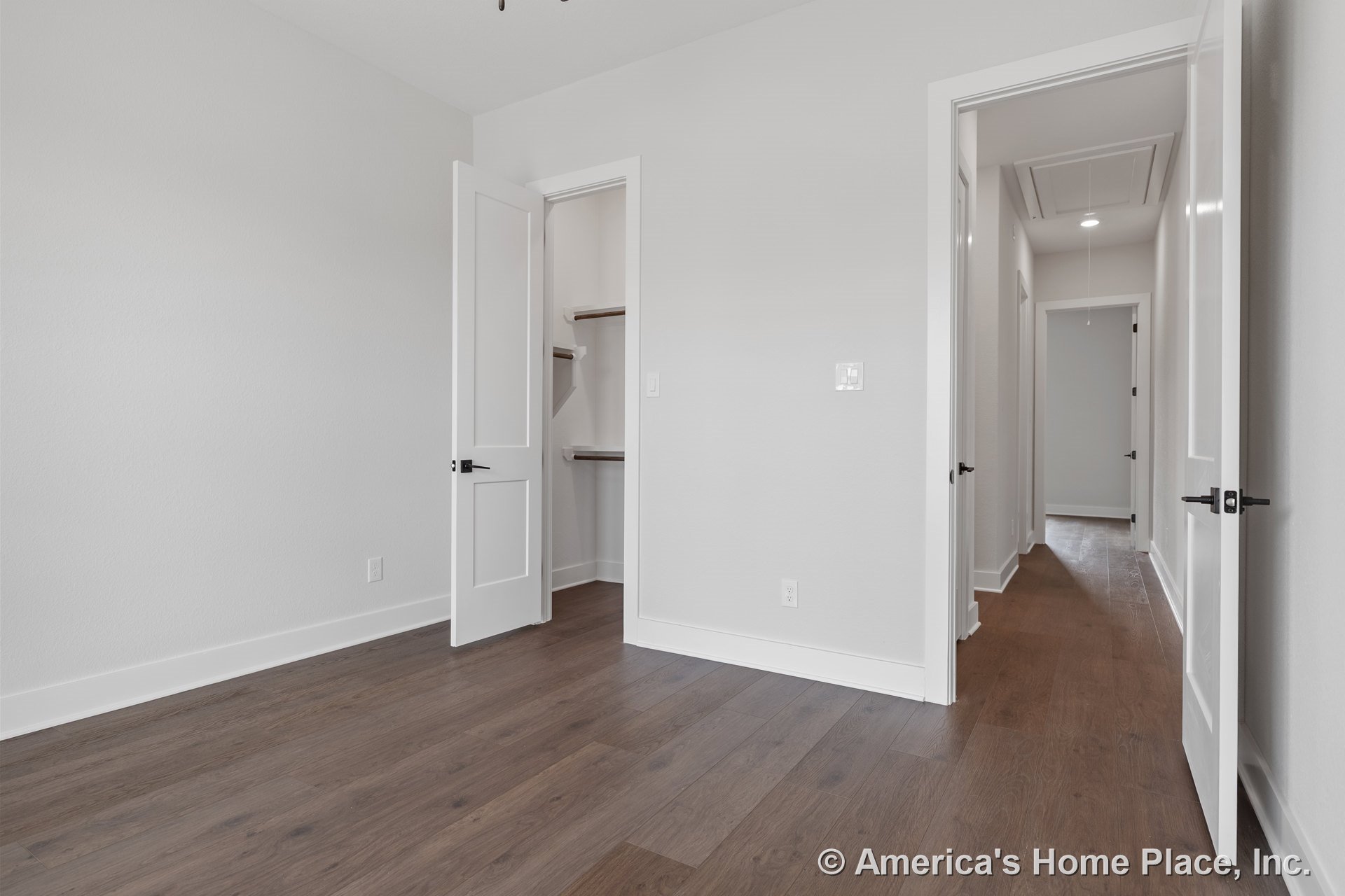 Bedroom with wood plank flooring, white baseboards and trim, neutral wall paint, paneled interior doors, walk-in closet featuring built-in shelving, and recessed ceiling light