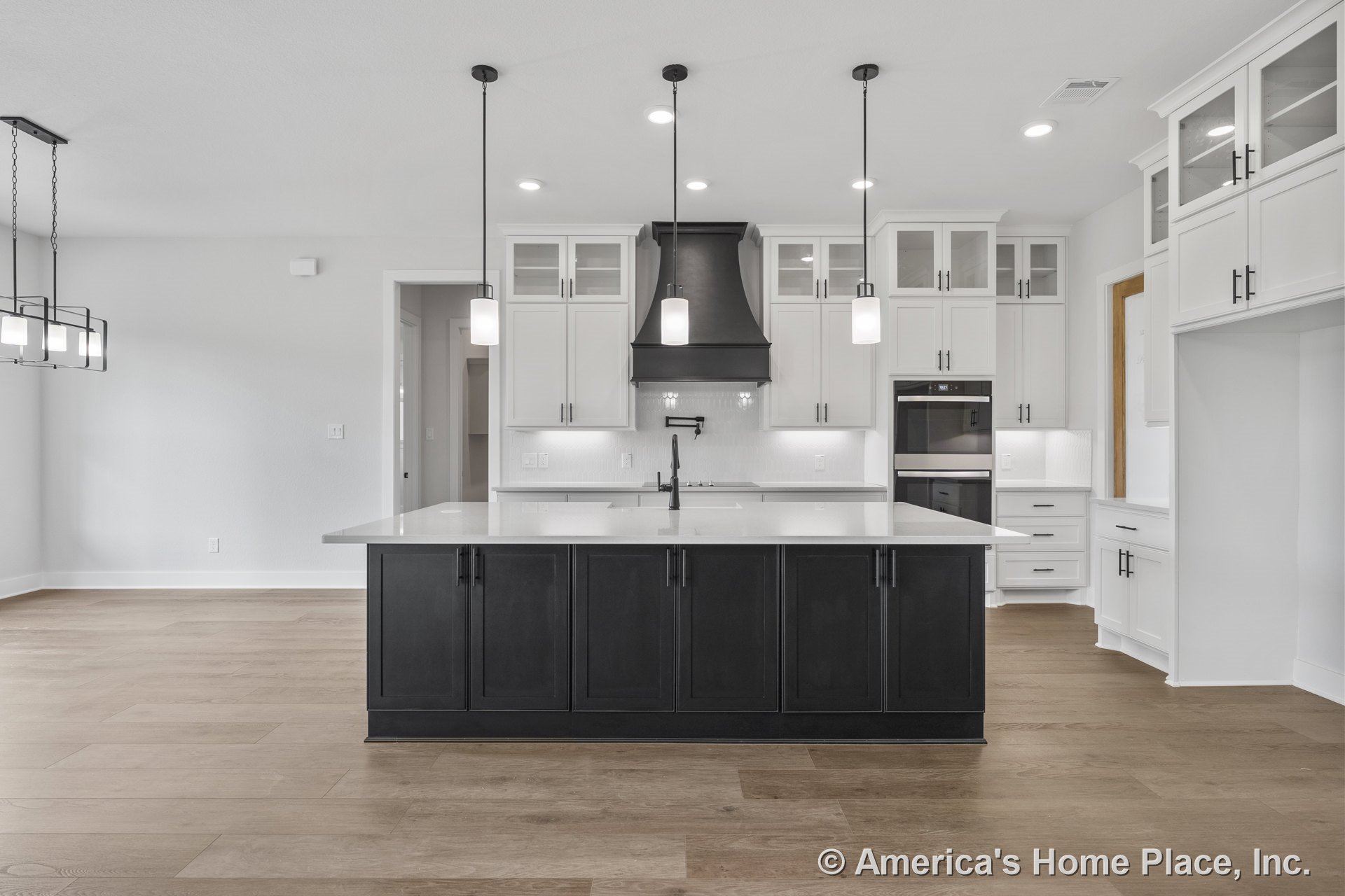 Spacious kitchen with black island, white upper cabinets, quartz countertops, modern pendant lights, wood plank flooring, double wall oven, tile backsplash, built-in cabinetry