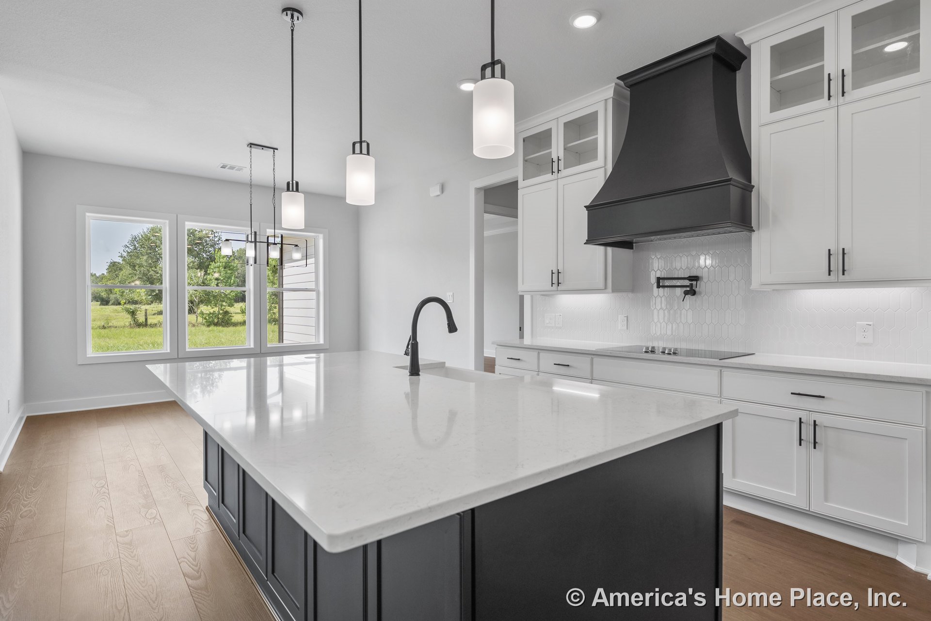 Spacious kitchen with a large quartz island, white shaker cabinets, black range hood, hexagonal tile backsplash, pendant lights, hardwood flooring, built-in faucet, under-cabinet