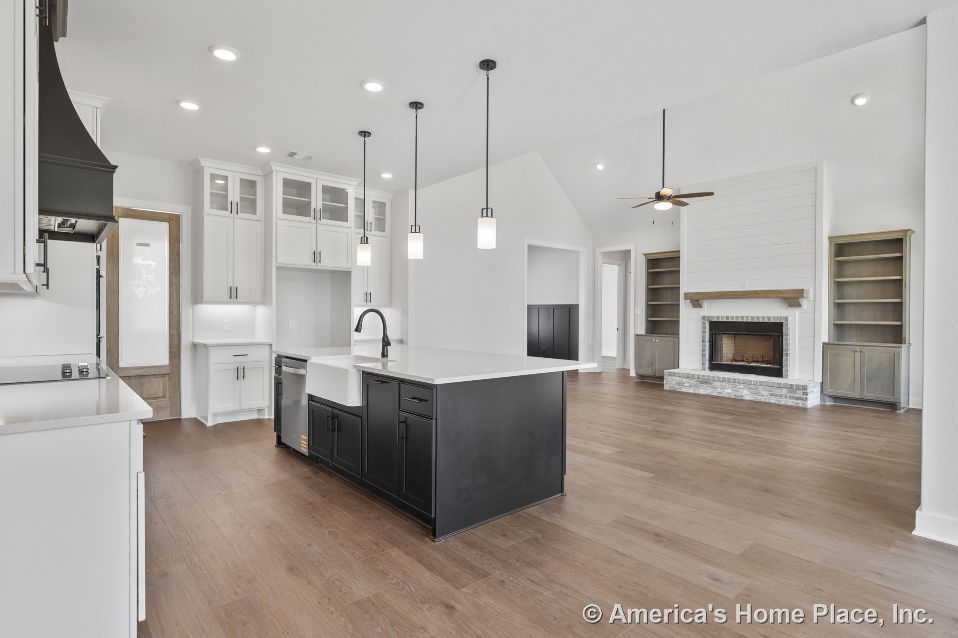 Open concept kitchen and living area with white upper cabinets featuring glass doors, black quartz island with farmhouse sink and modern faucet, pendant lights above island