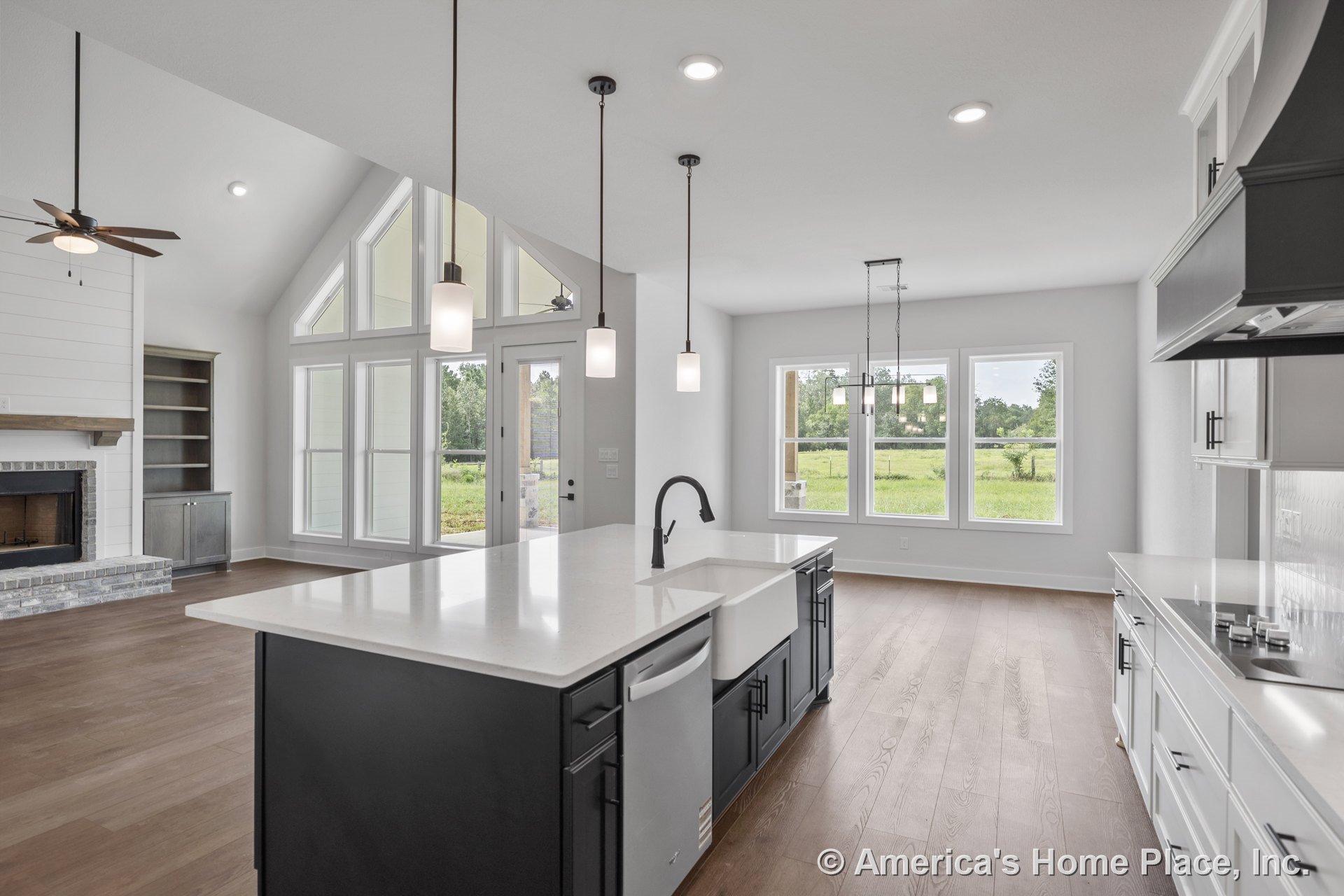 Open kitchen and living area with vaulted ceiling, recessed and pendant lighting, large island featuring quartz countertops and farmhouse sink, white shaker cabinets, brick