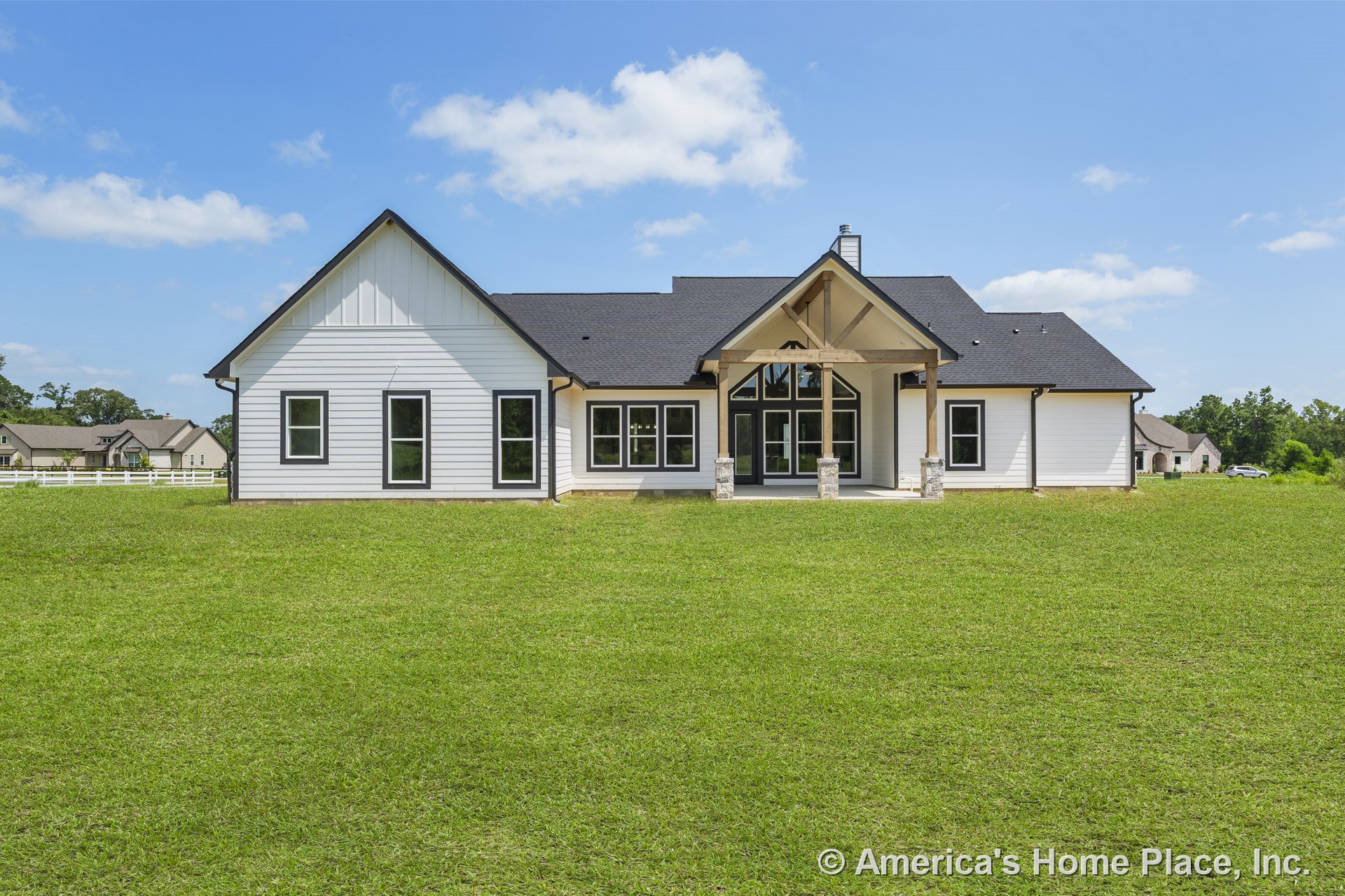 White horizontal siding with black-trimmed windows, covered front porch featuring wood beams and stone column bases, gabled roof, and multiple large windows at the front entry.
