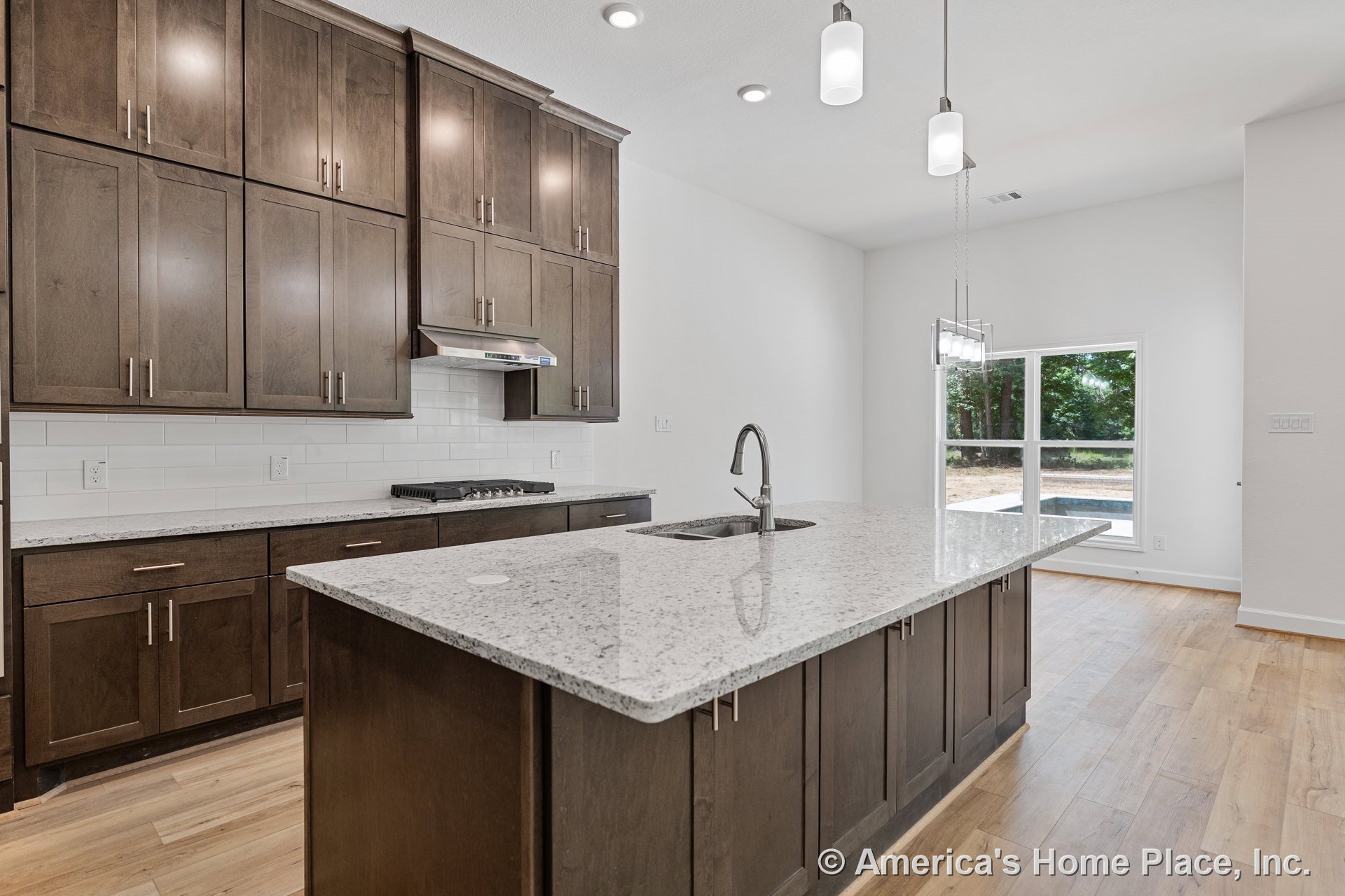 Dark wood cabinetry kitchen with large granite island, white subway tile backsplash, built-in gas cooktop, pendant and recessed lighting, stainless steel faucet, hardwood flooring