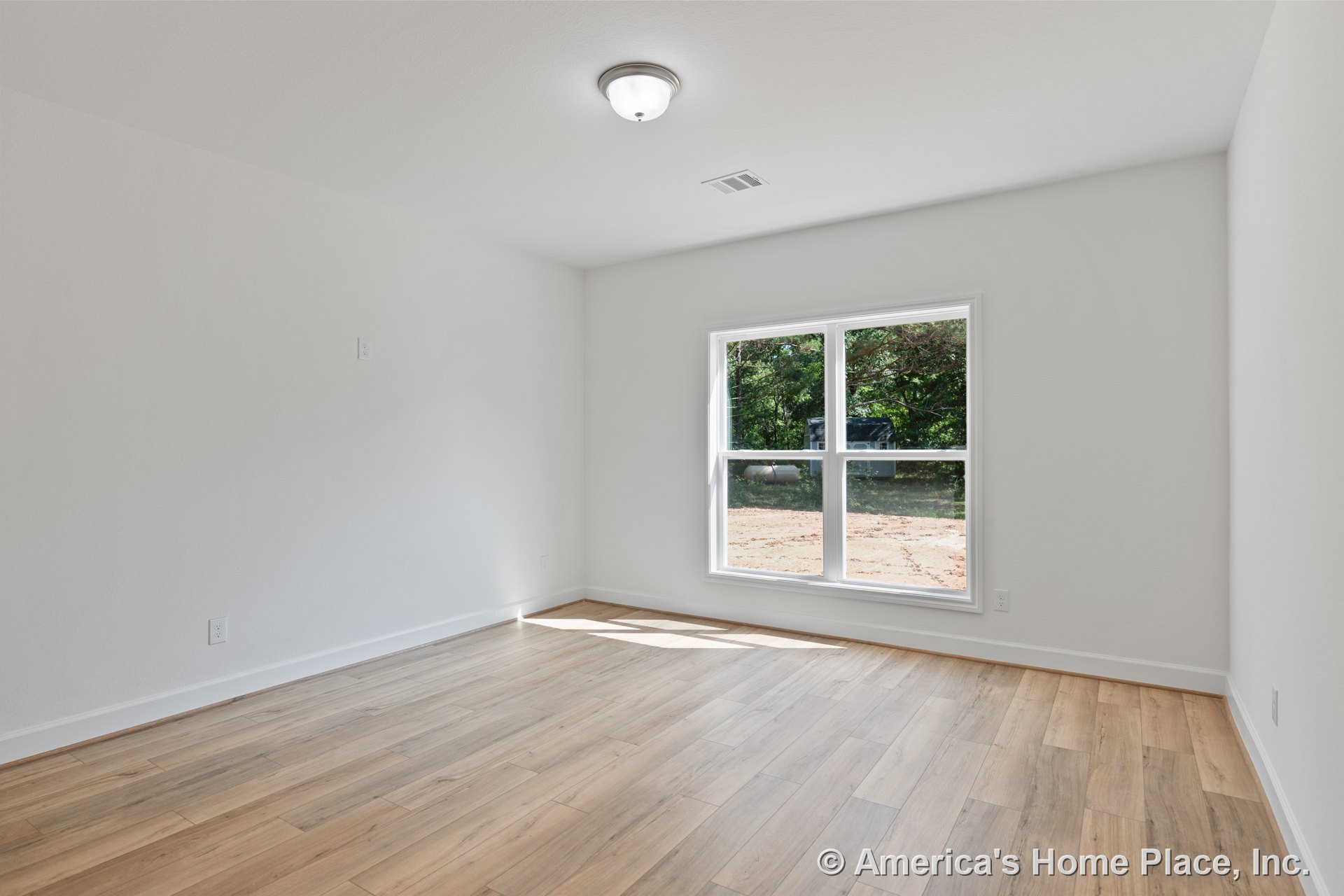 Large double windows with white trim fill a rectangular bedroom with natural light, highlighting light wood plank flooring, white walls, baseboard trim, and a flush mount ceiling