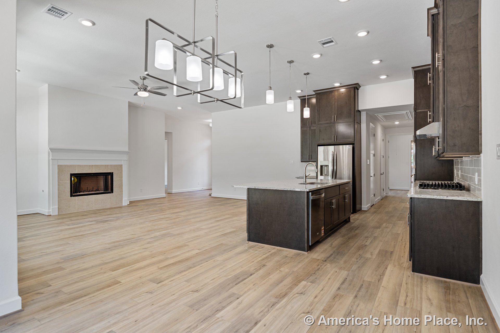 Open kitchen and living area with dark wood cabinetry, quartz island countertop, wide plank wood flooring, built-in tile fireplace surround, modern pendant lights, recessed