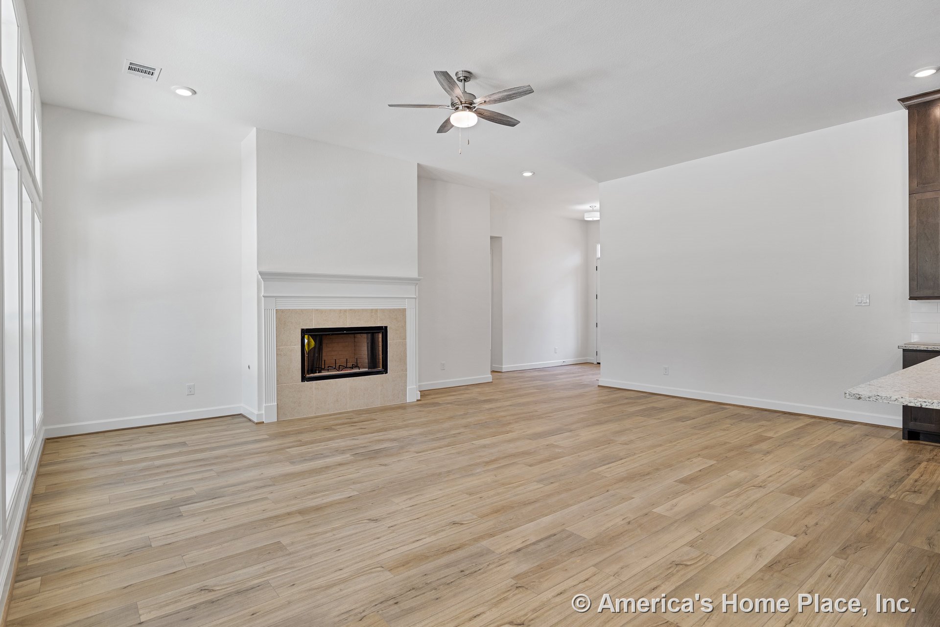 Tile-surround fireplace with wood-look plank flooring, ceiling fan featuring built-in lighting, white trim and baseboards, large windows, and open concept layout.